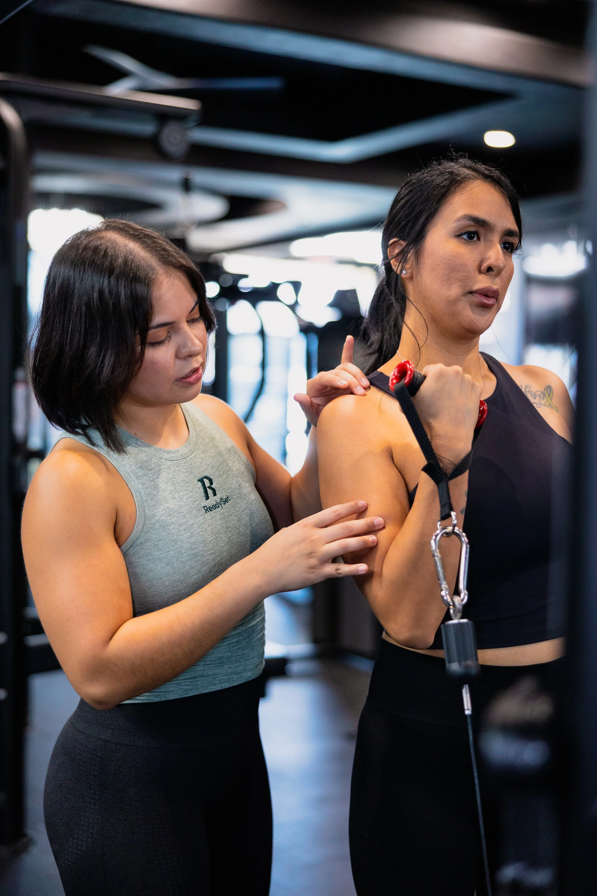A personal trainer assists a woman with her workout by guiding her on how to use a resistance band, in a gym setting.