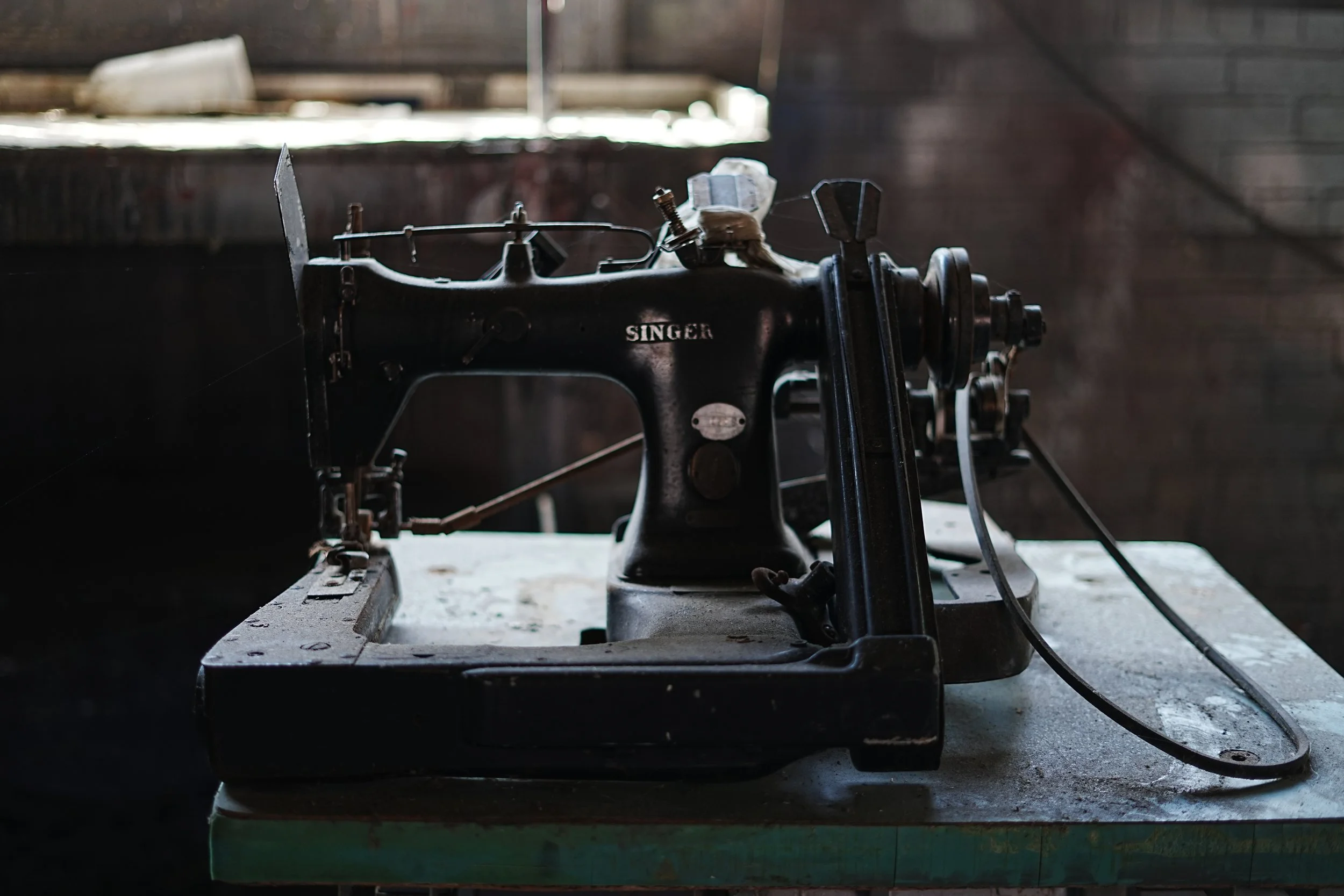 Old black Singer sewing machine with rust and dust, placed on a worn wooden table in a dimly lit room.