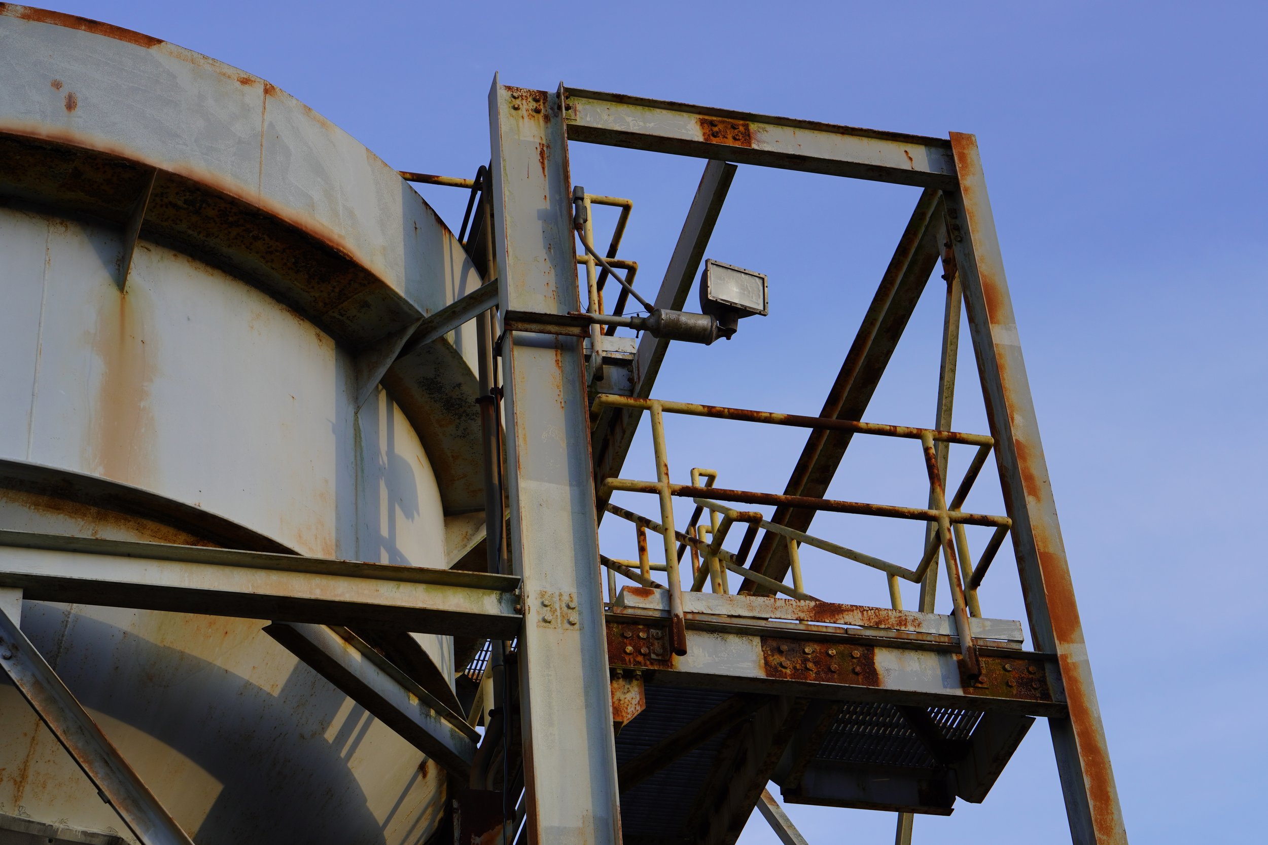 Close-up of an old, rusted, metal industrial structure with stairs and railings against a clear blue sky.