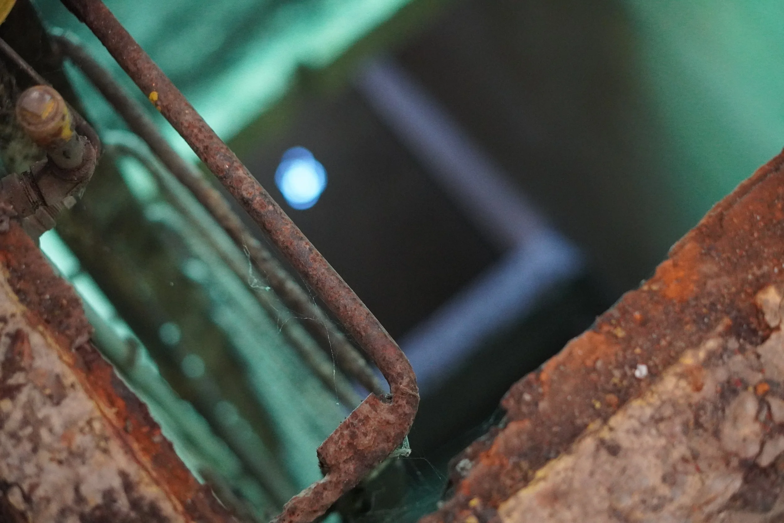 Close-up of rusted metal bars and a green object seen through a hole in a rusted metal surface.