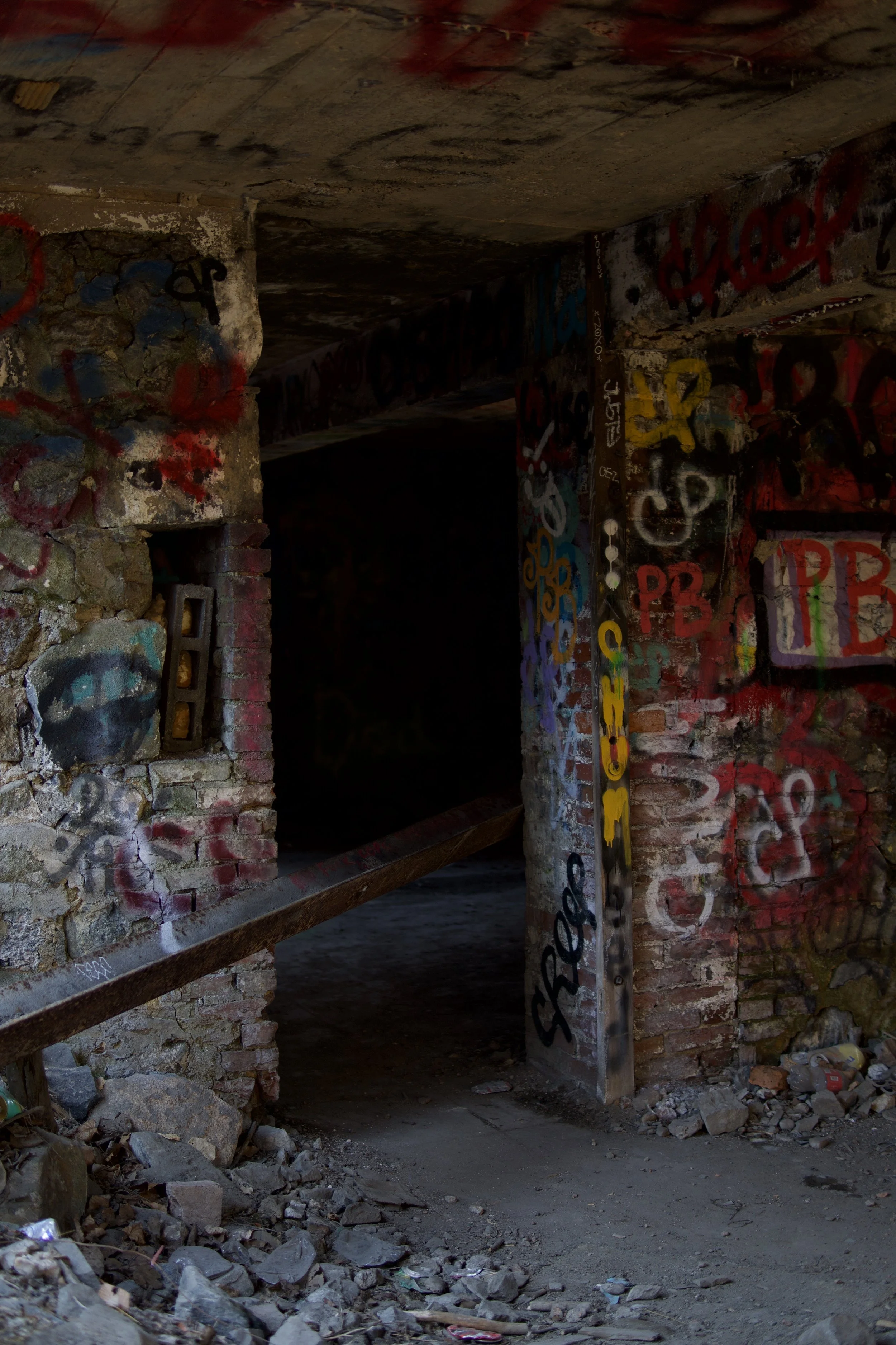 Underground tunnel with graffitied brick walls and debris on the ground.