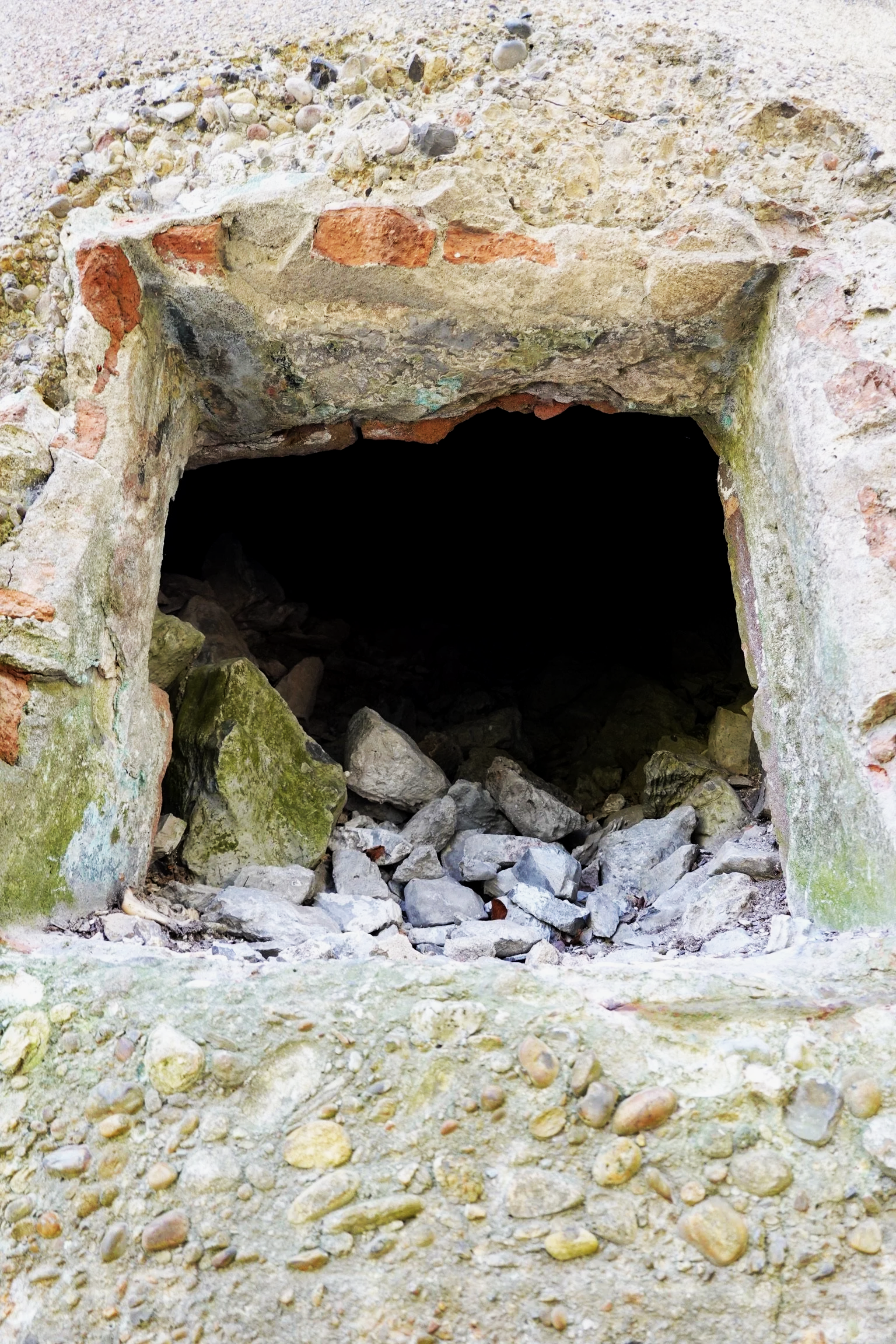 Small underground tunnel or cellar with a round opening, built with bricks and stones, surrounded by gravel and rocks.