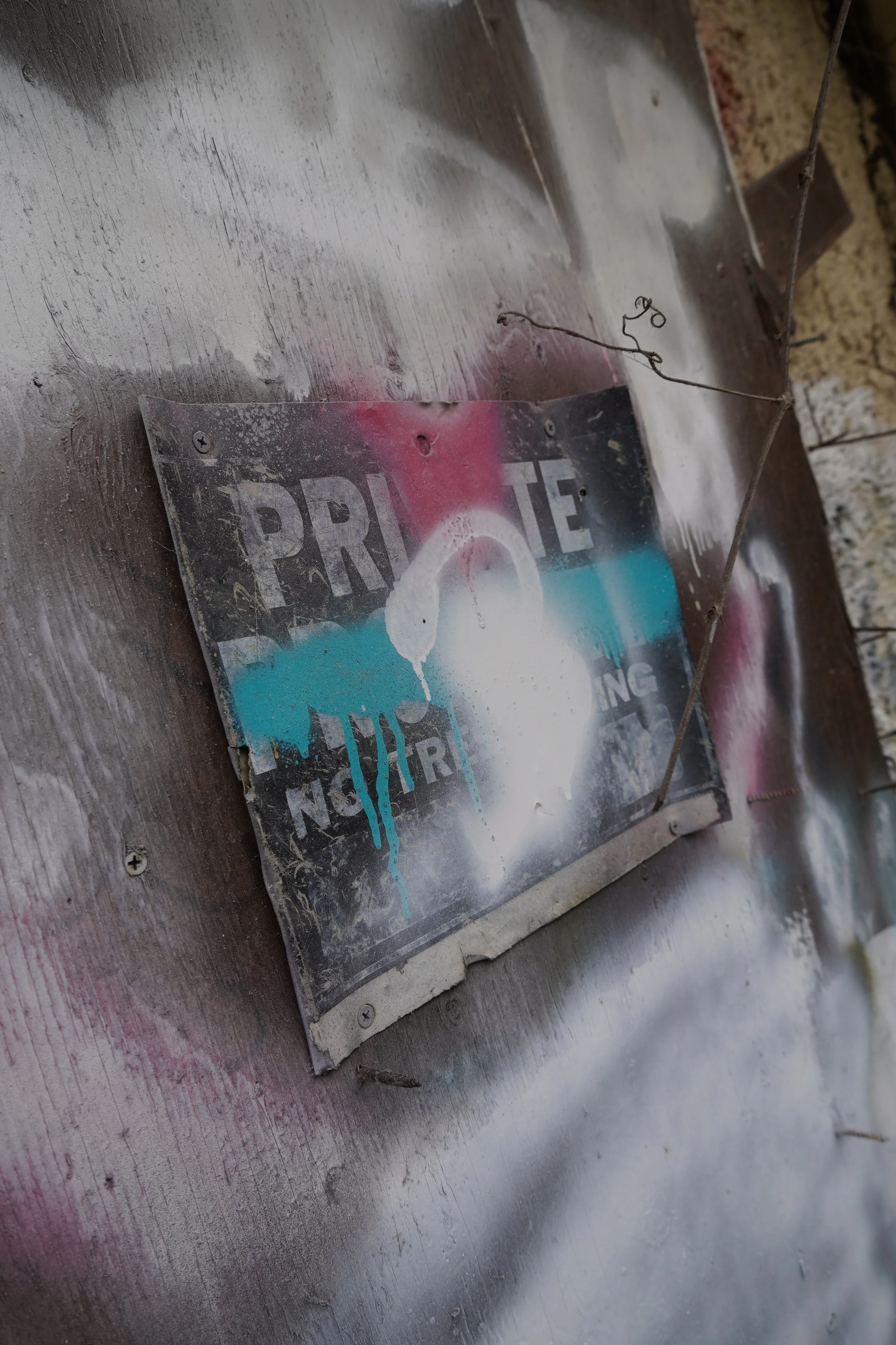 A weathered, partially torn and faded sign attached to a metallic surface, with spray paint splatters nearby.