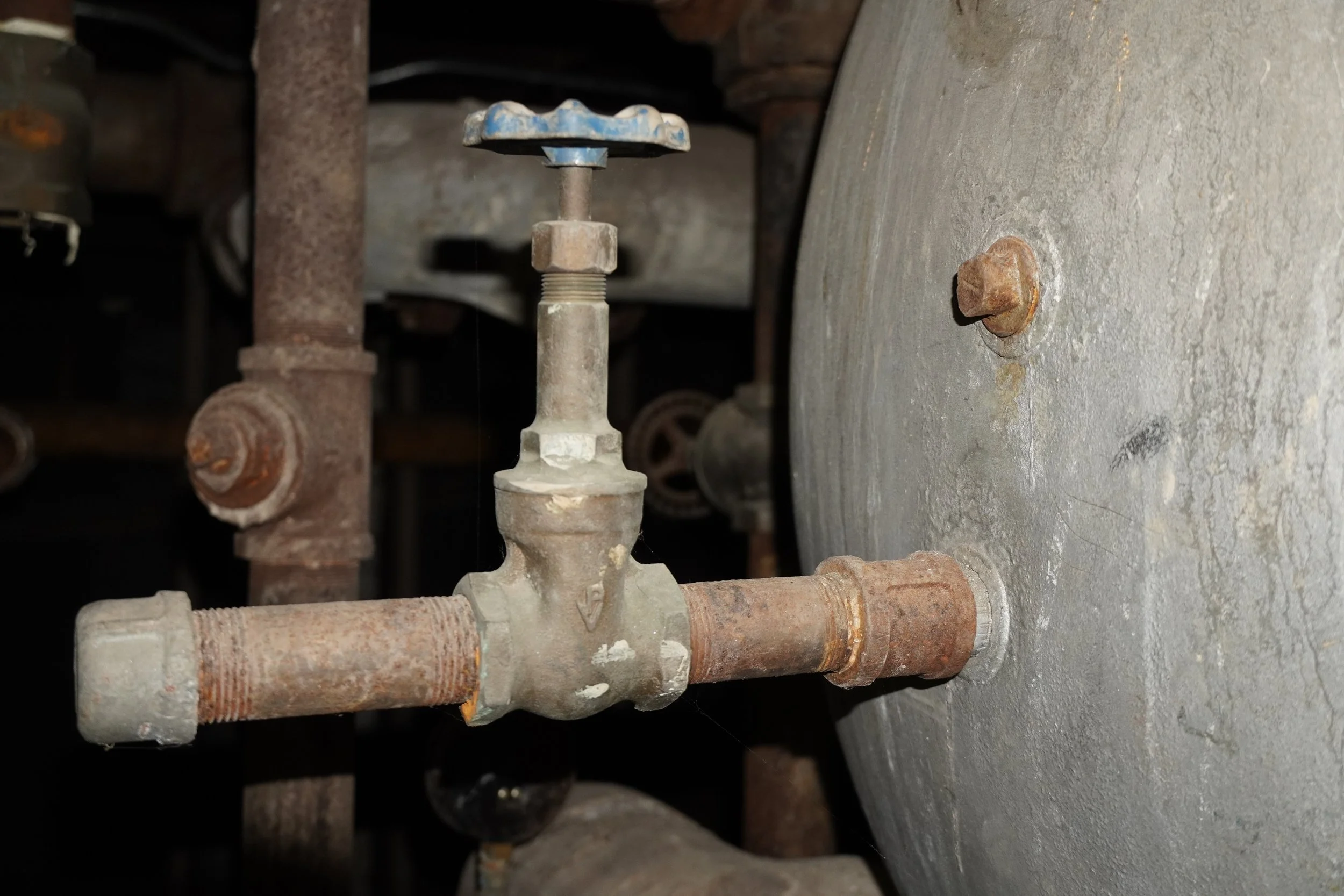 Close-up of old, rusty pipe fittings and valves against a concrete wall, showing signs of corrosion and wear.
