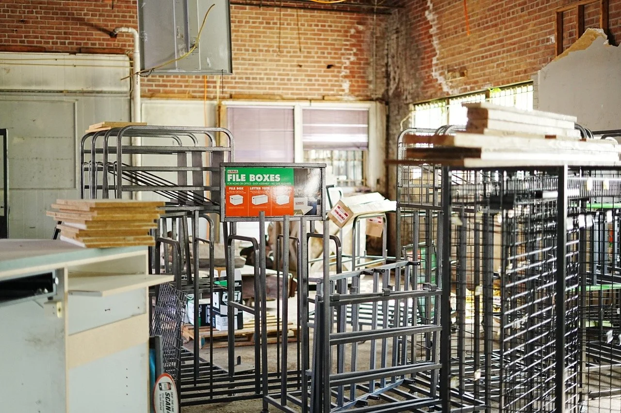 Empty wire mesh carts and file boxes in a warehouse with exposed brick walls and windows.