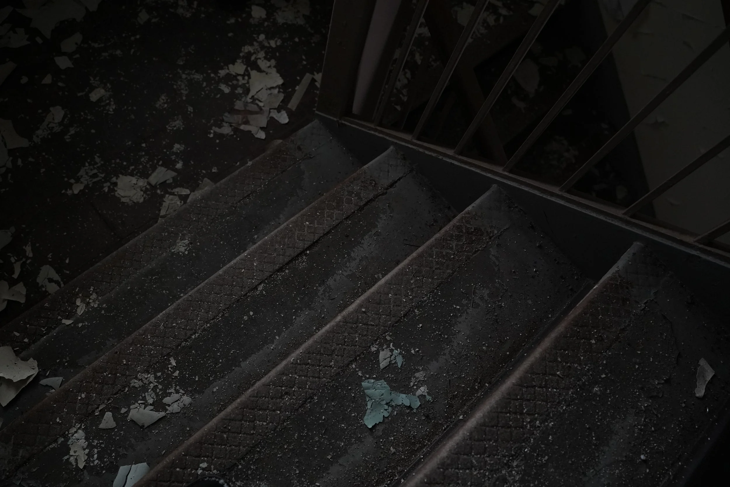 Dark staircase with debris and shattered paint chips scattered on the steps and floor, metal railing on one side.