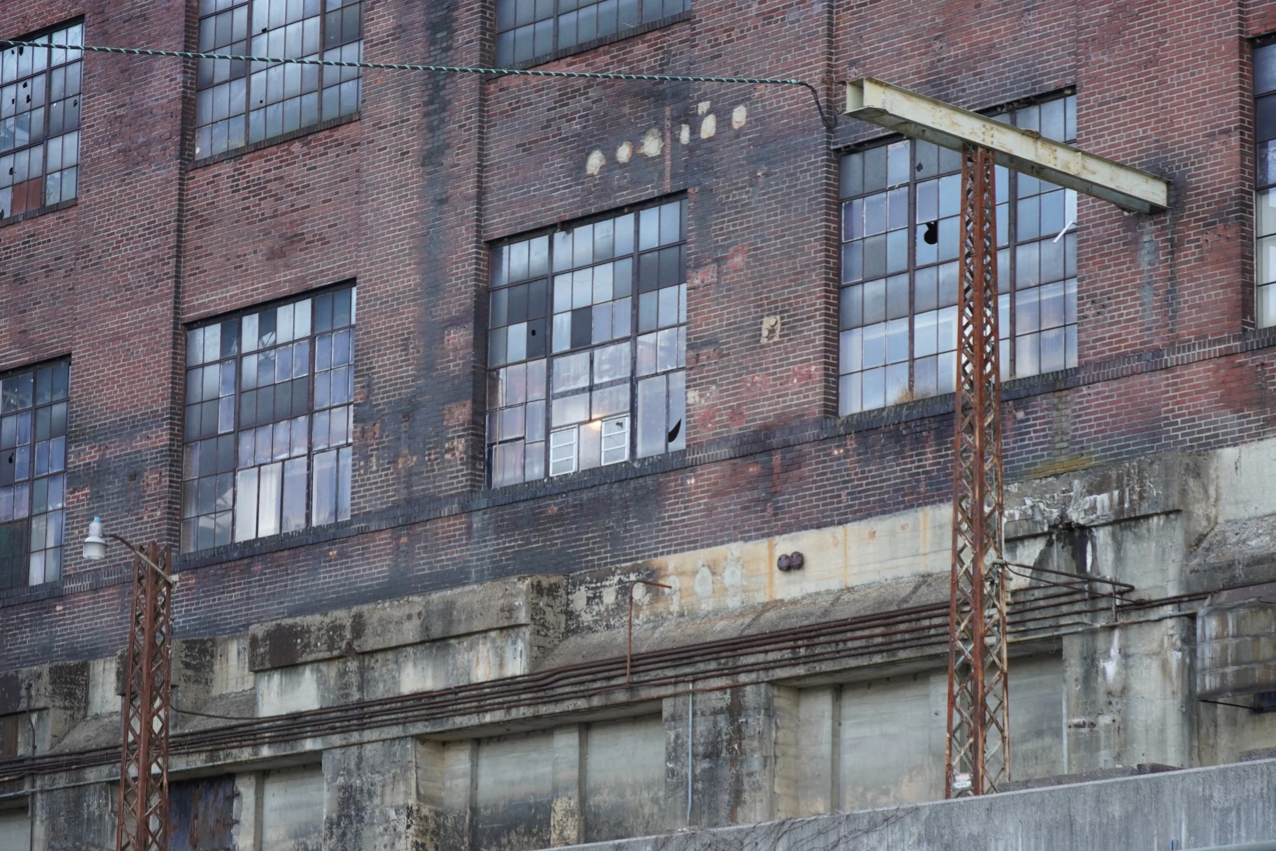 Close-up of an old brick building with broken and missing window panes, some windows boarded up or missing glass, and rusty structural elements.