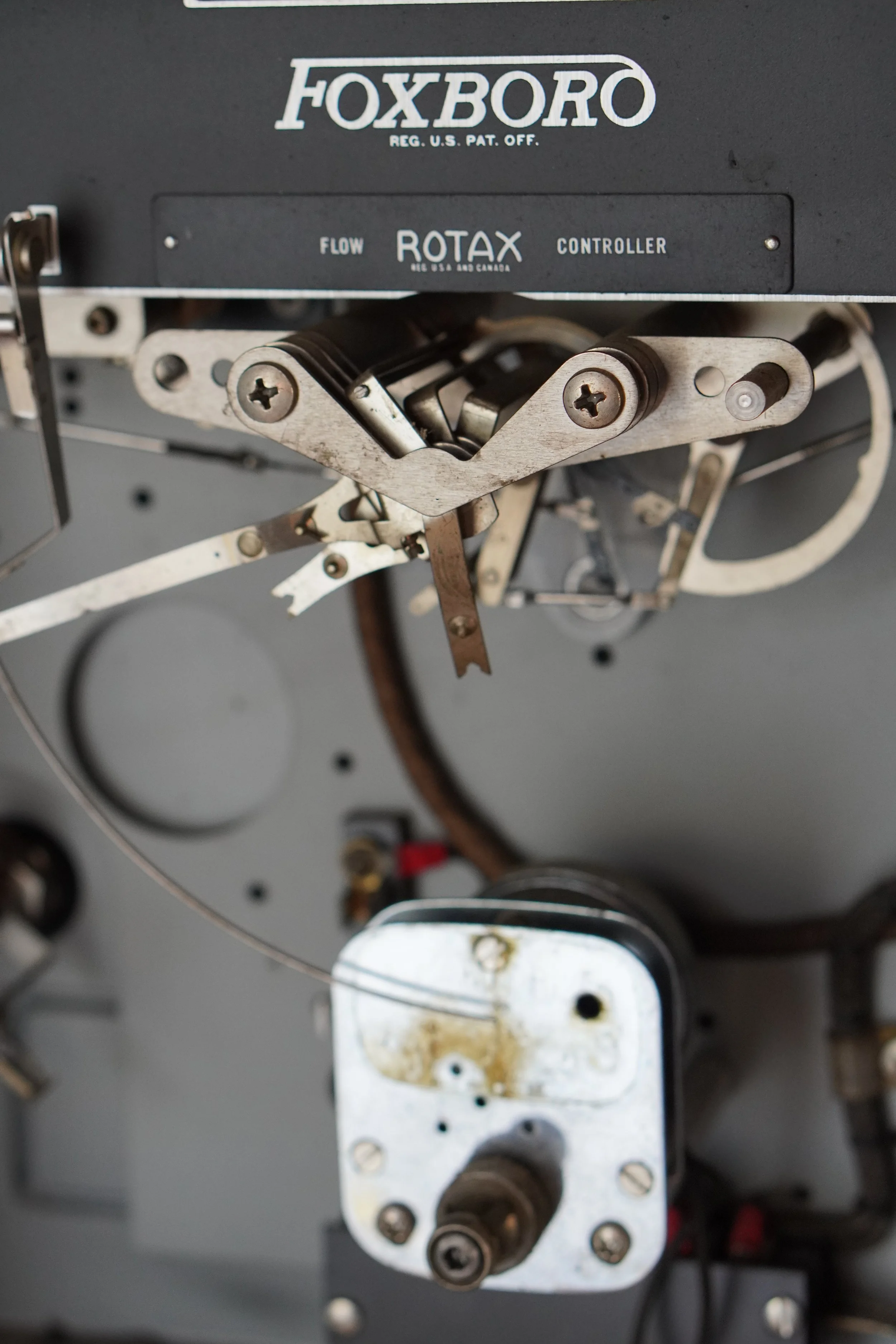 Close-up of a vintage mechanical device with metal components, screws, and a labeled panel reading 'FOXBORO' and 'ROTAX CONTROLER'.