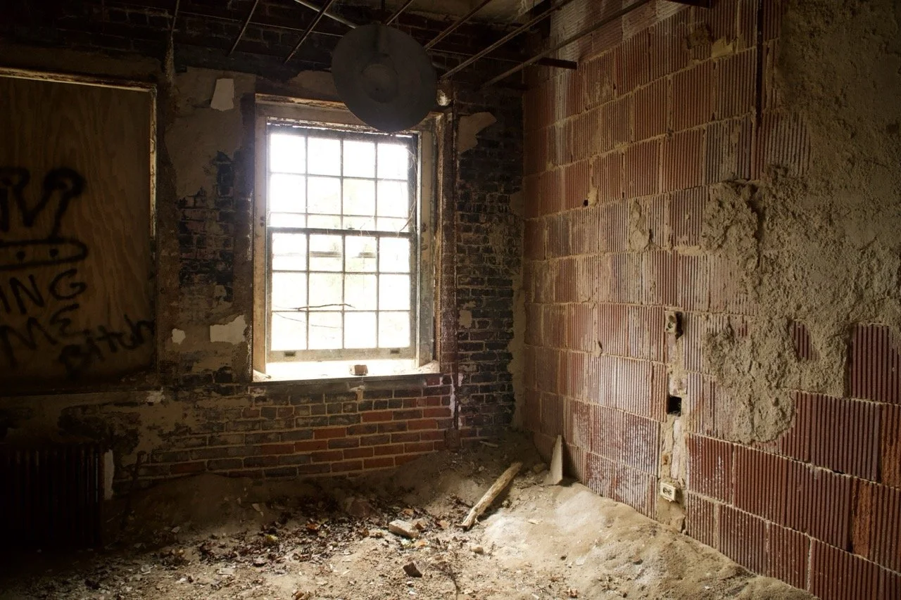 An unfinished room with exposed brick walls, a brick window frame, and construction debris on the floor.