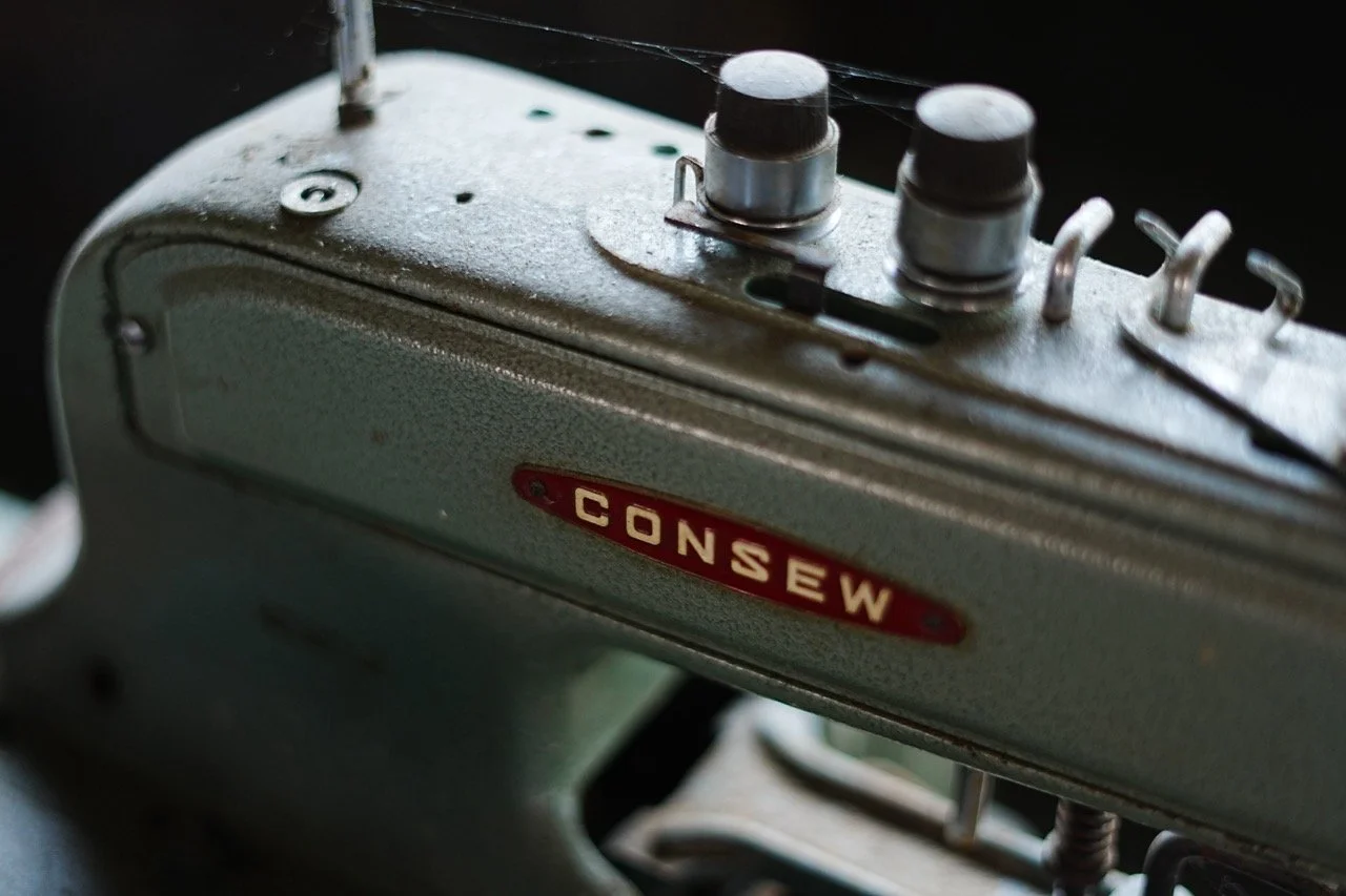 Close-up of a vintage Consew sewing machine, showing metal components and a red label with the brand name.