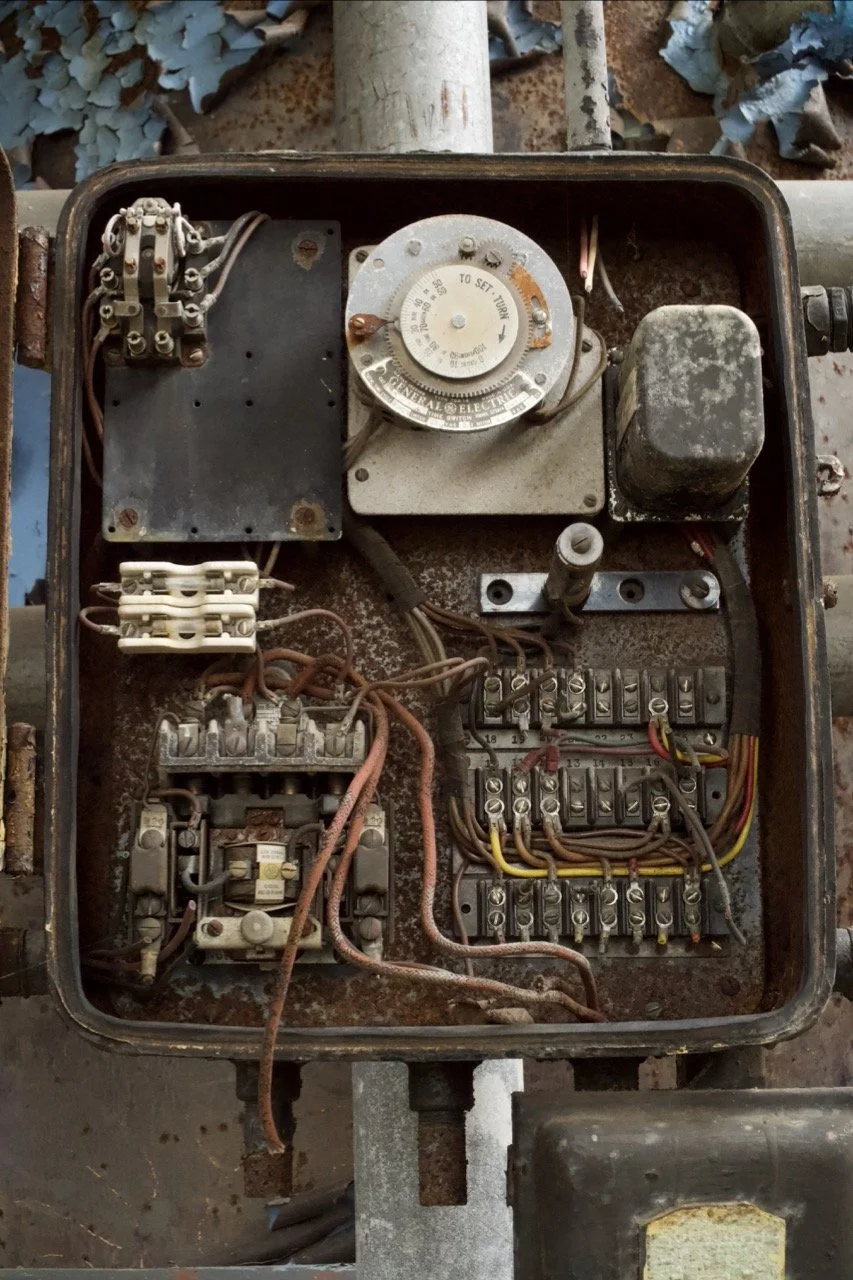 An old, rusty electrical control box with various wires, switches, and a timer dial inside.