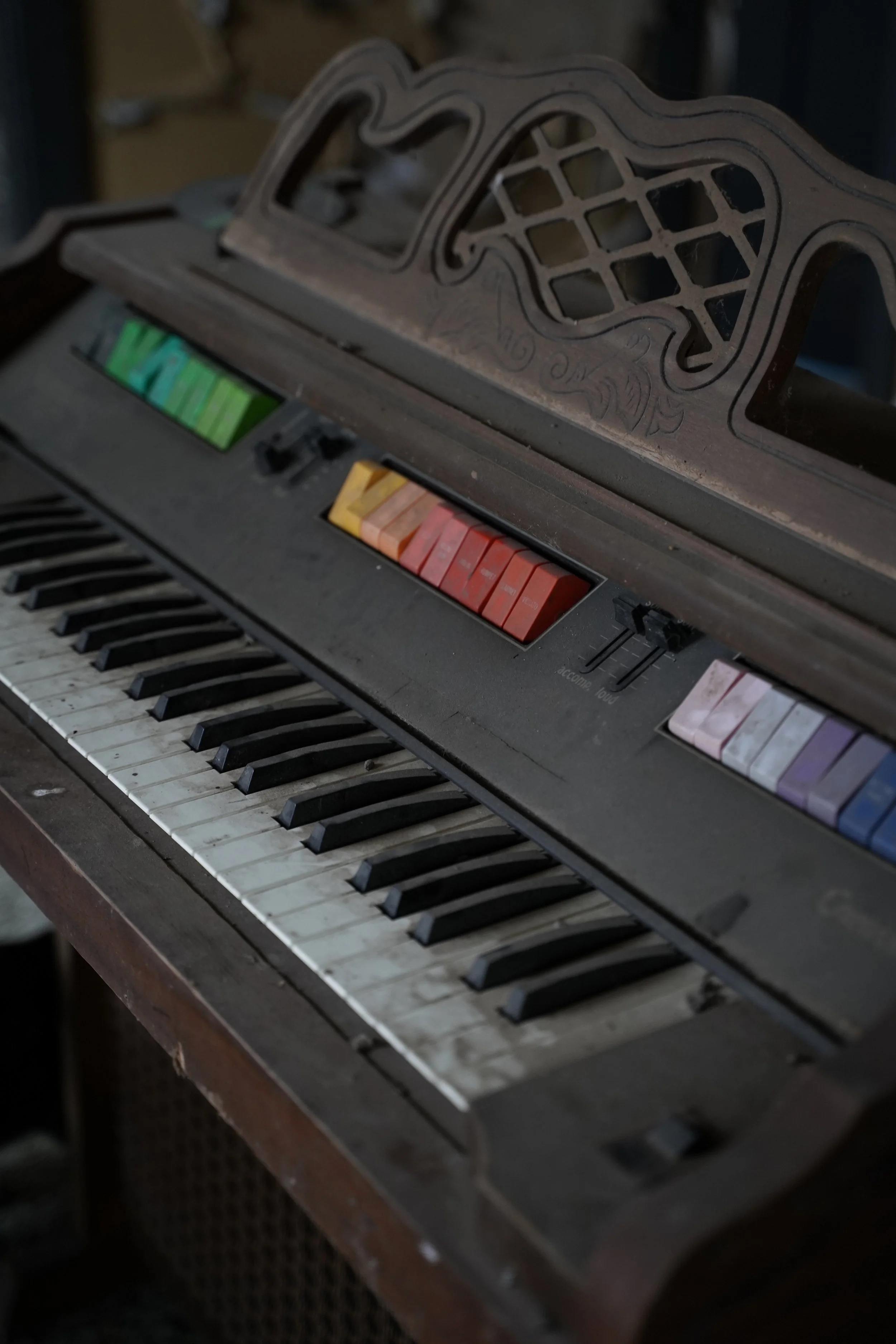 An old, dusty electronic keyboard with a broken cover on top and worn keys, resting on a dark wooden surface.
