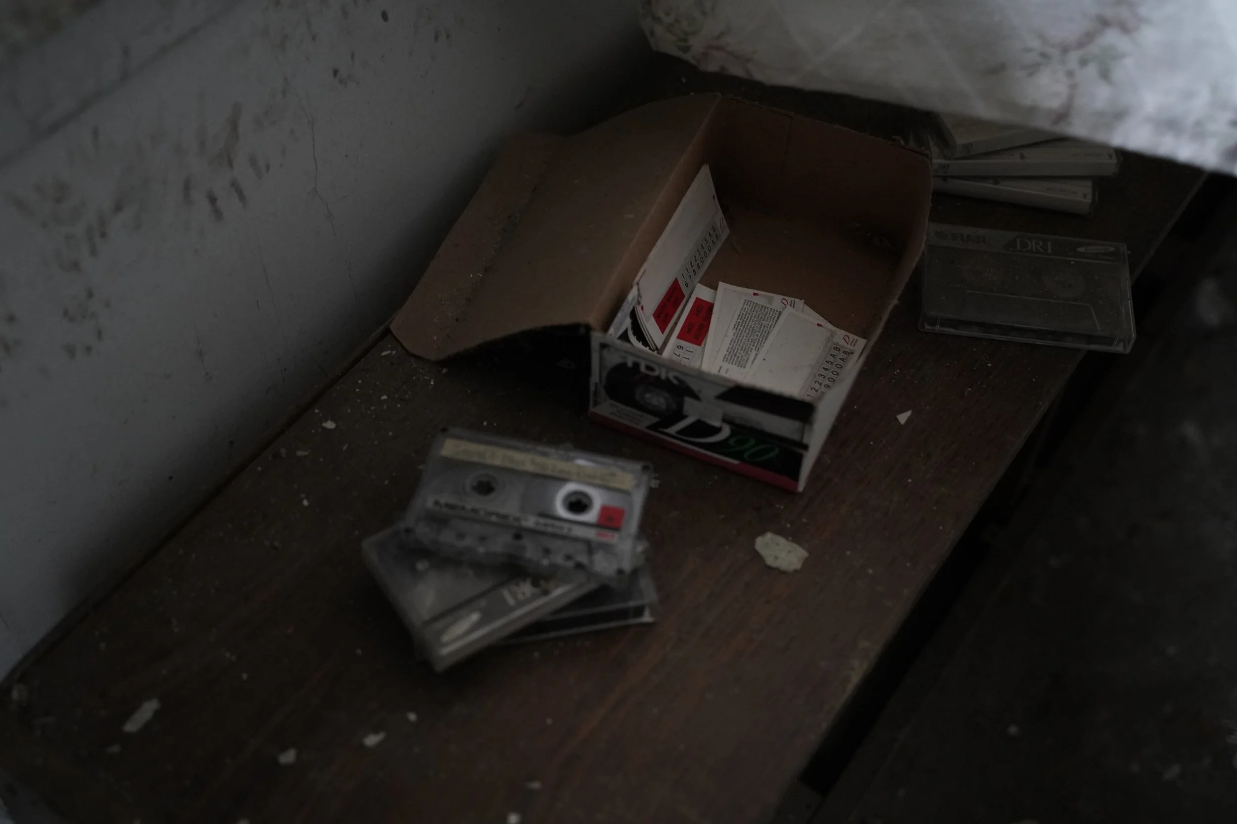 A dark, dusty storage area with cardboard boxes, film cases, and scattered debris on a wooden surface.