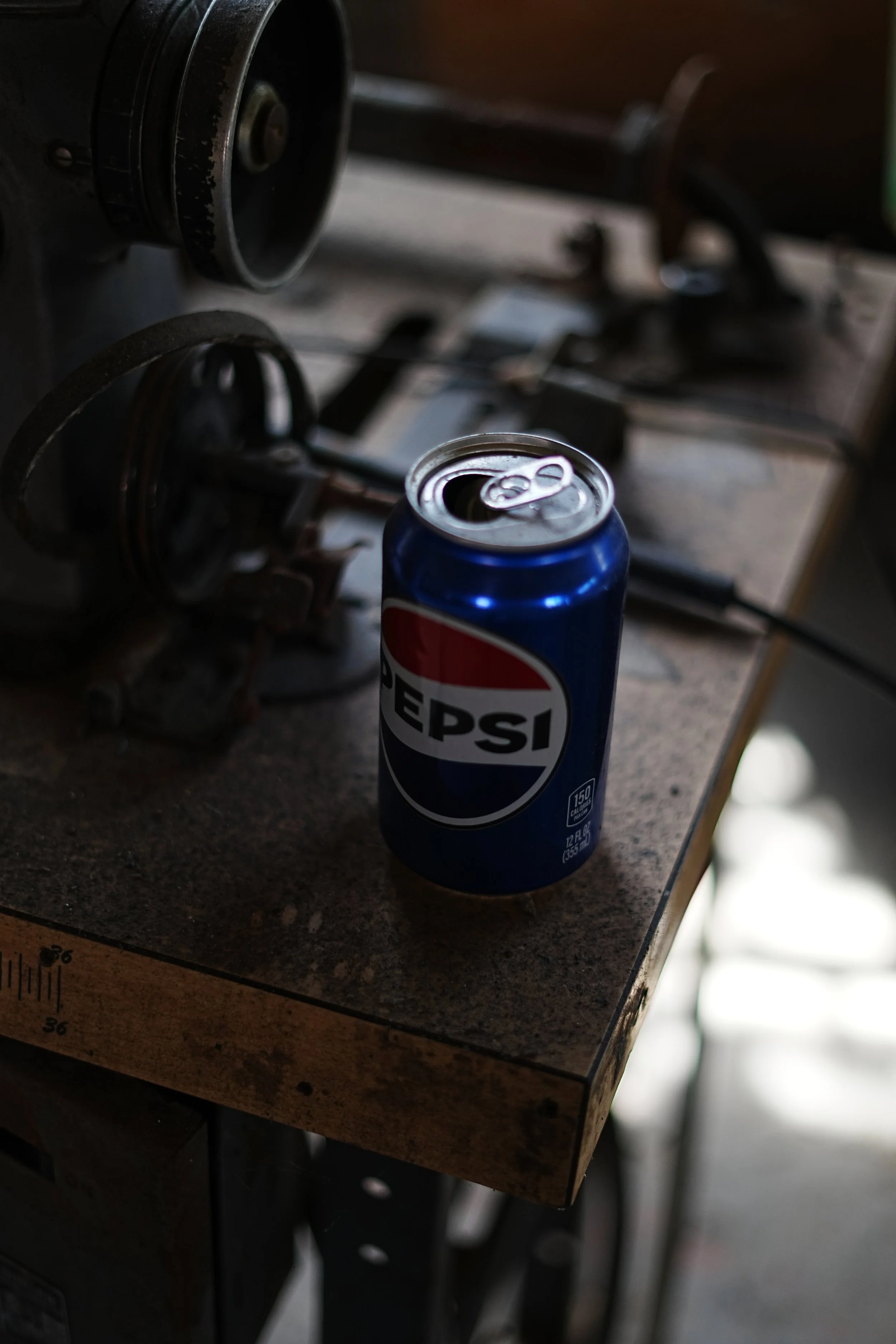 Soda can of Pepsi on a cluttered workbench, with a black and metal wrench, a drill, and other tools in the background.