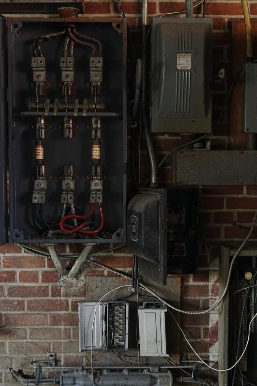 Electrical breaker panel and wiring mounted on a brick wall.
