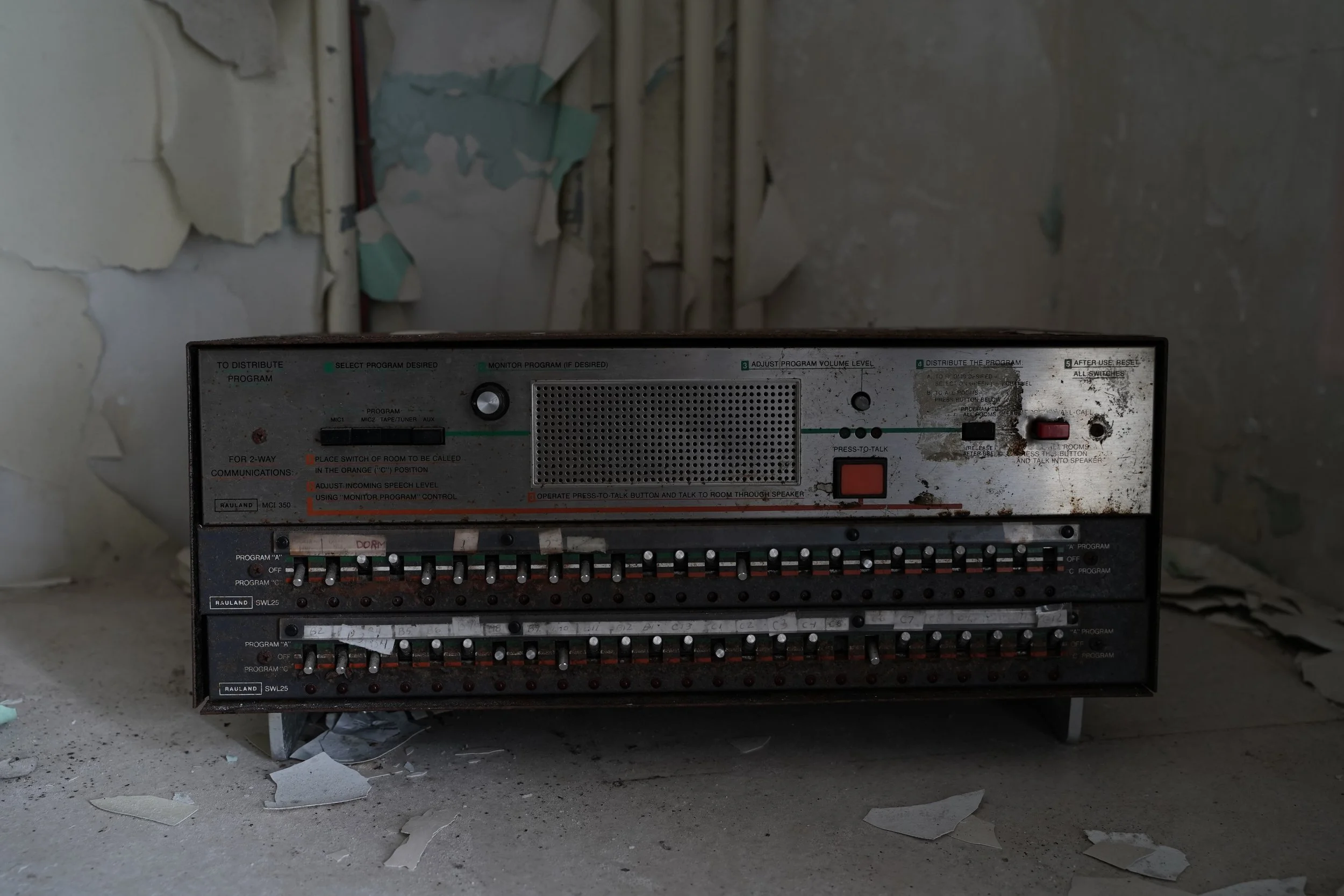 An electrical control panel with multiple switches and labels, set against a damaged and peeling wall in a dusty environment.