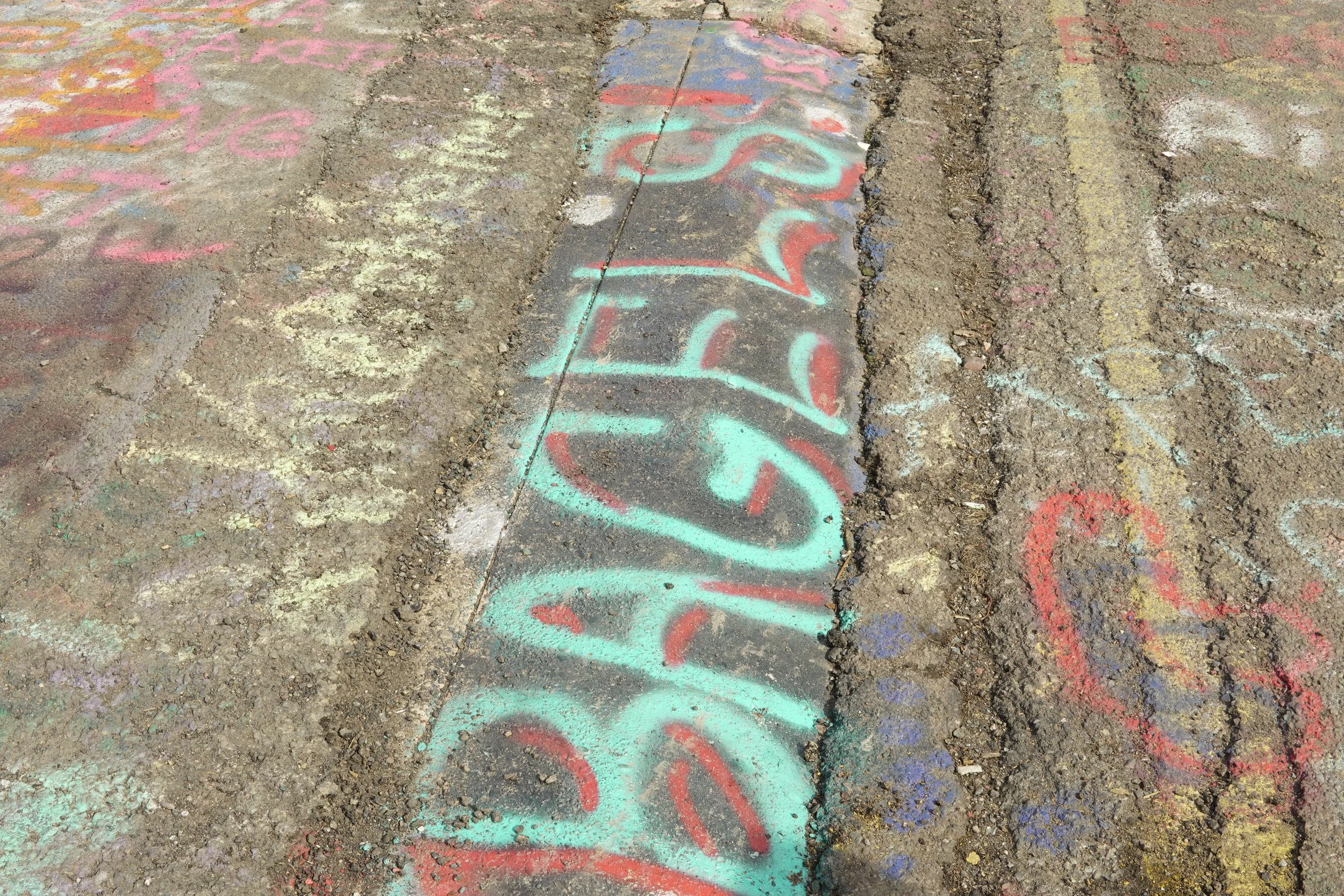 Colorful graffiti and chalk drawings on a cracked concrete sidewalk.
