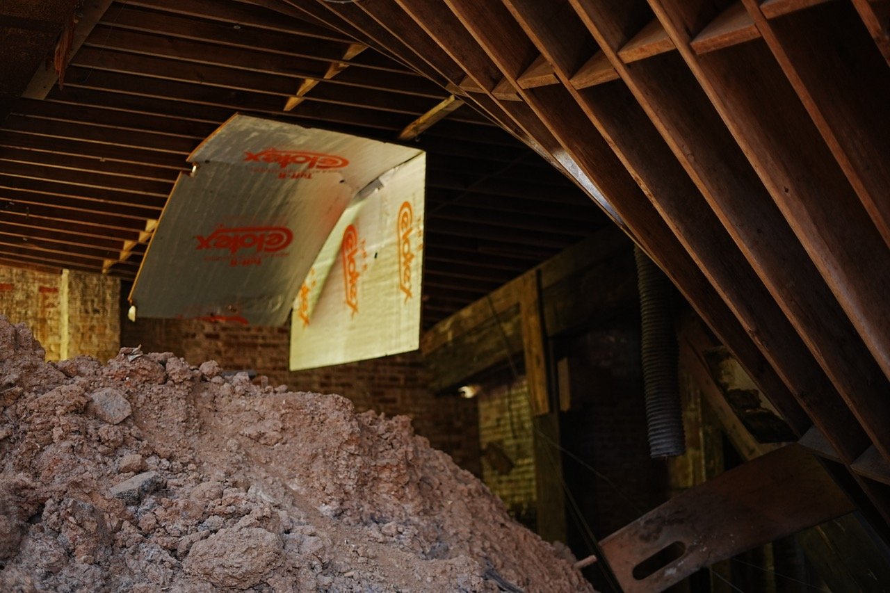 Construction site showing insulation material and a pile of dirt in an attic with exposed wooden beams.