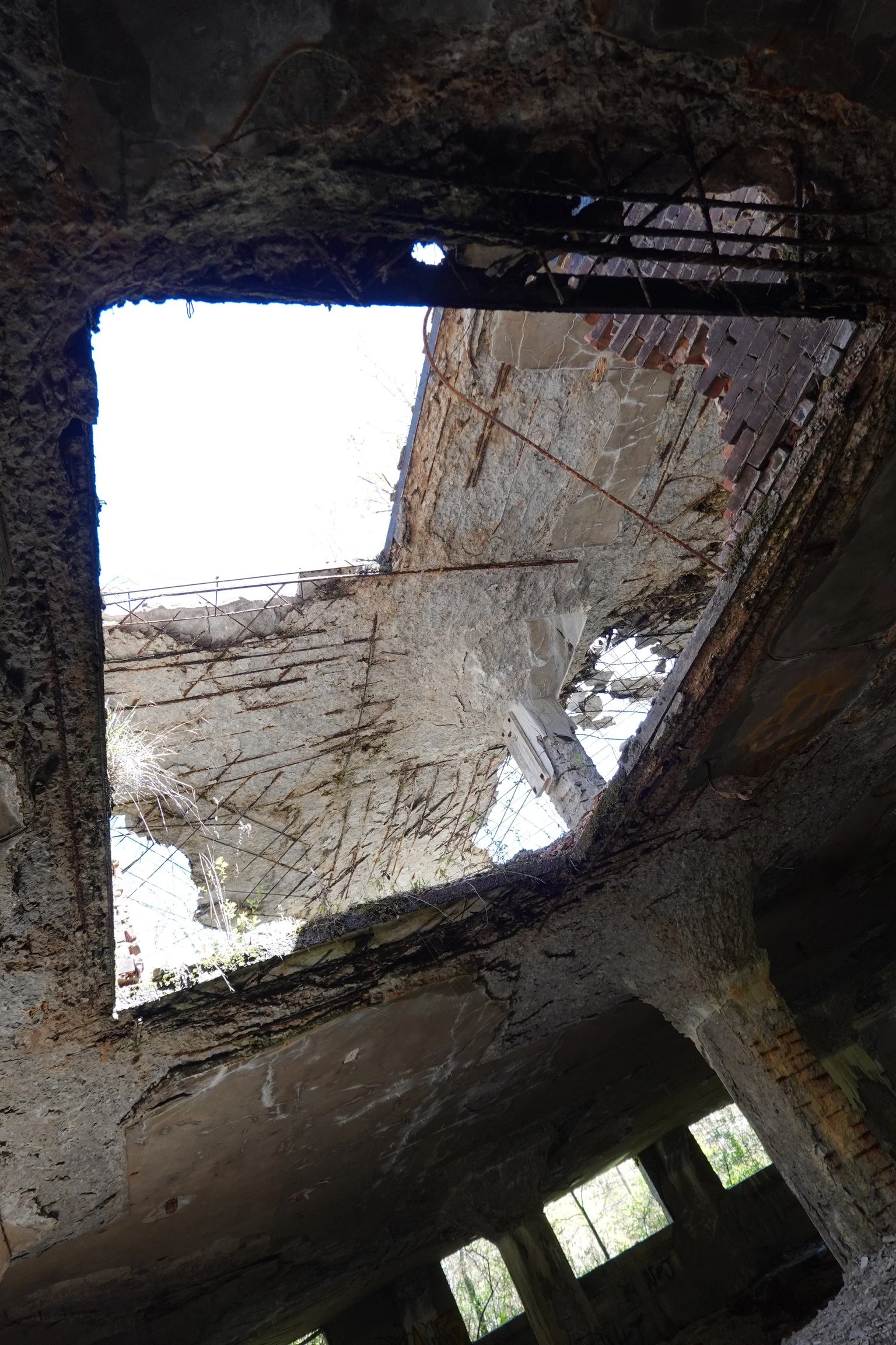 View of a hole in the roof of a crumbling, abandoned building showing the sky and some trees outside through the opening.