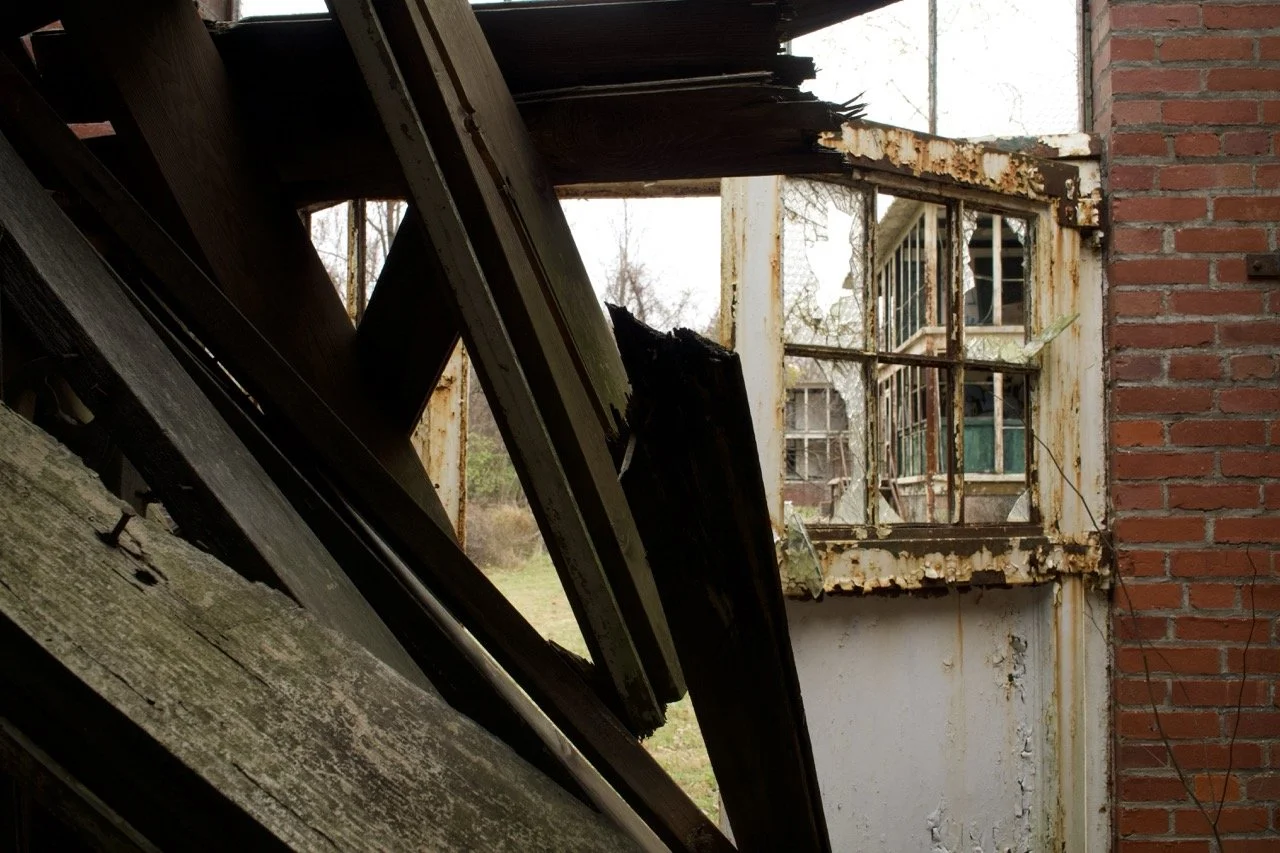 An abandoned, dilapidated building with broken and rotting window frames, peeling paint, and damaged wooden structures.