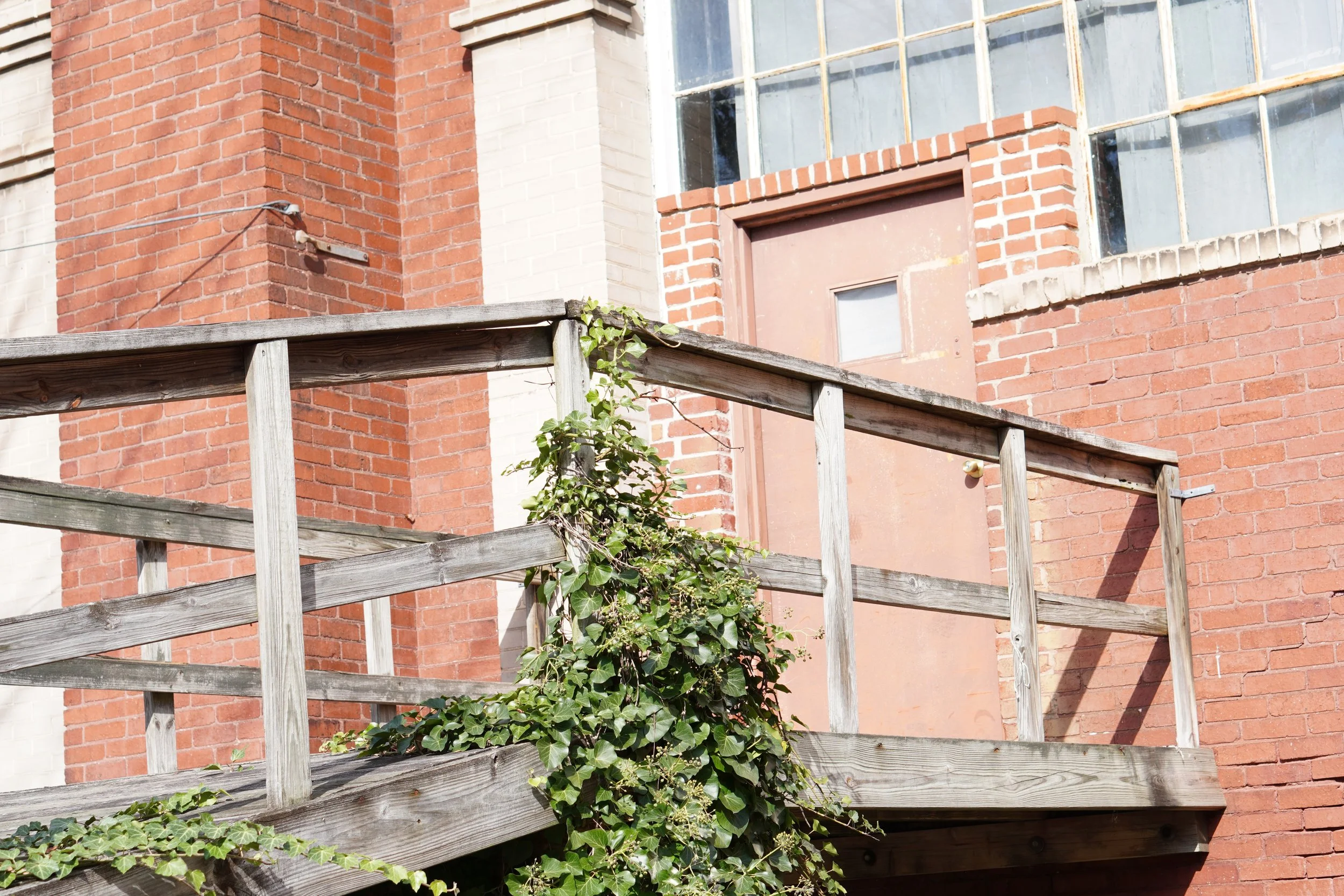 Close-up of a brick building with a wooden balcony and green ivy growing on it.
