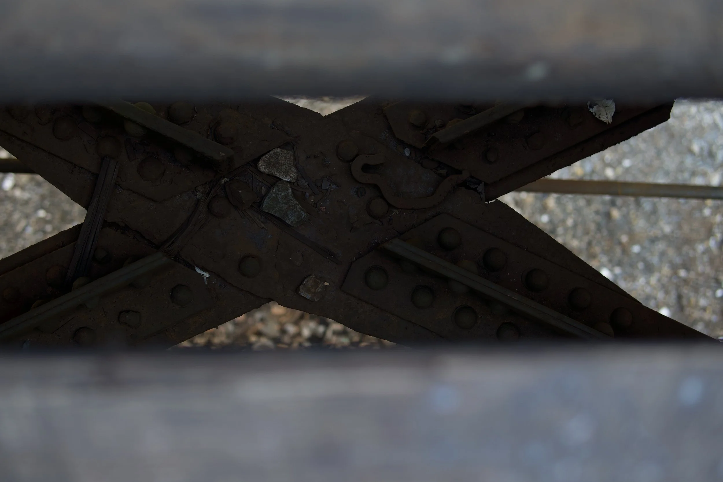 Close-up view under a railway bridge showing rusted metal beams and bolts, with blurred background.