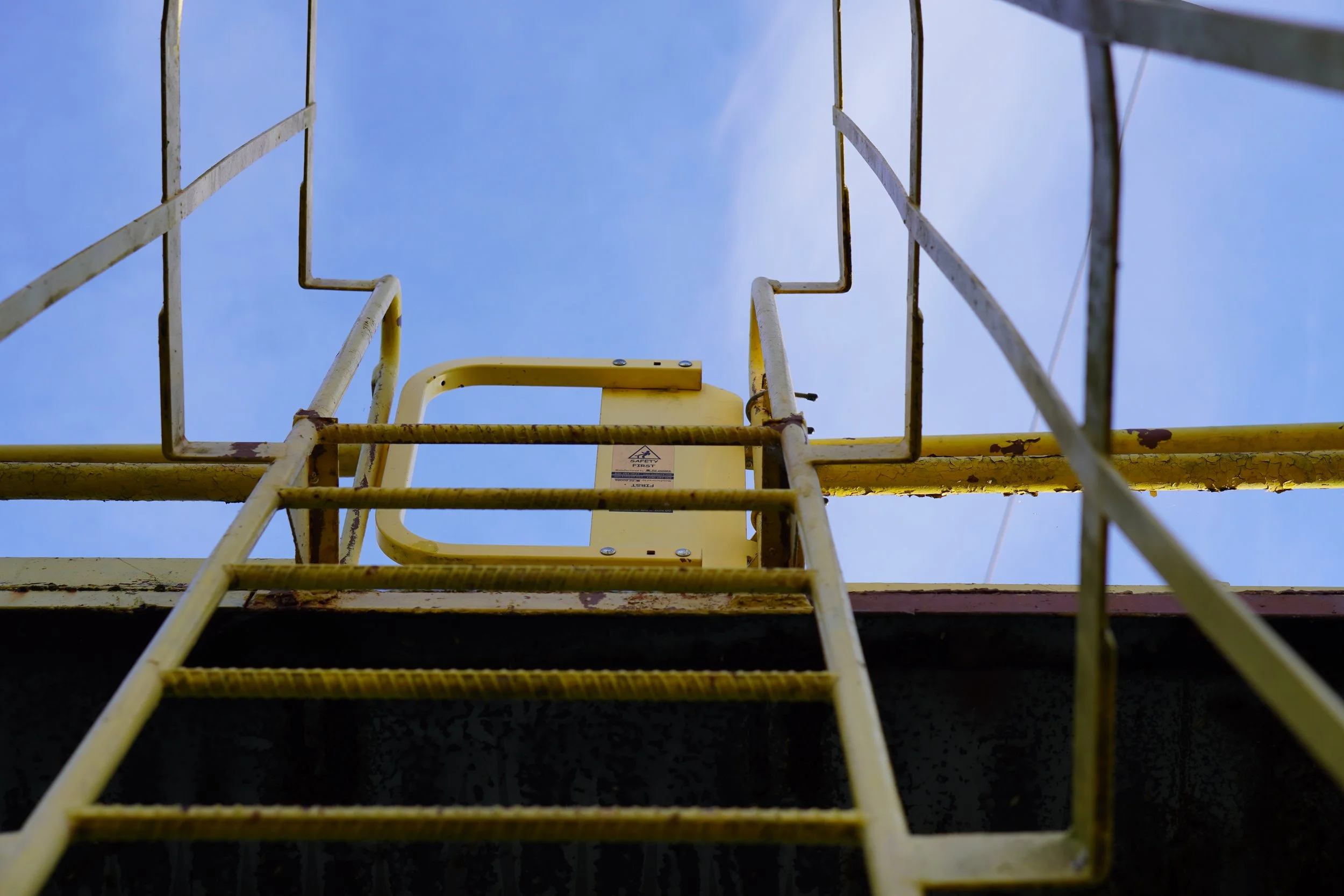 Looking up at the inside of a yellow ladder against a blue sky with some clouds.