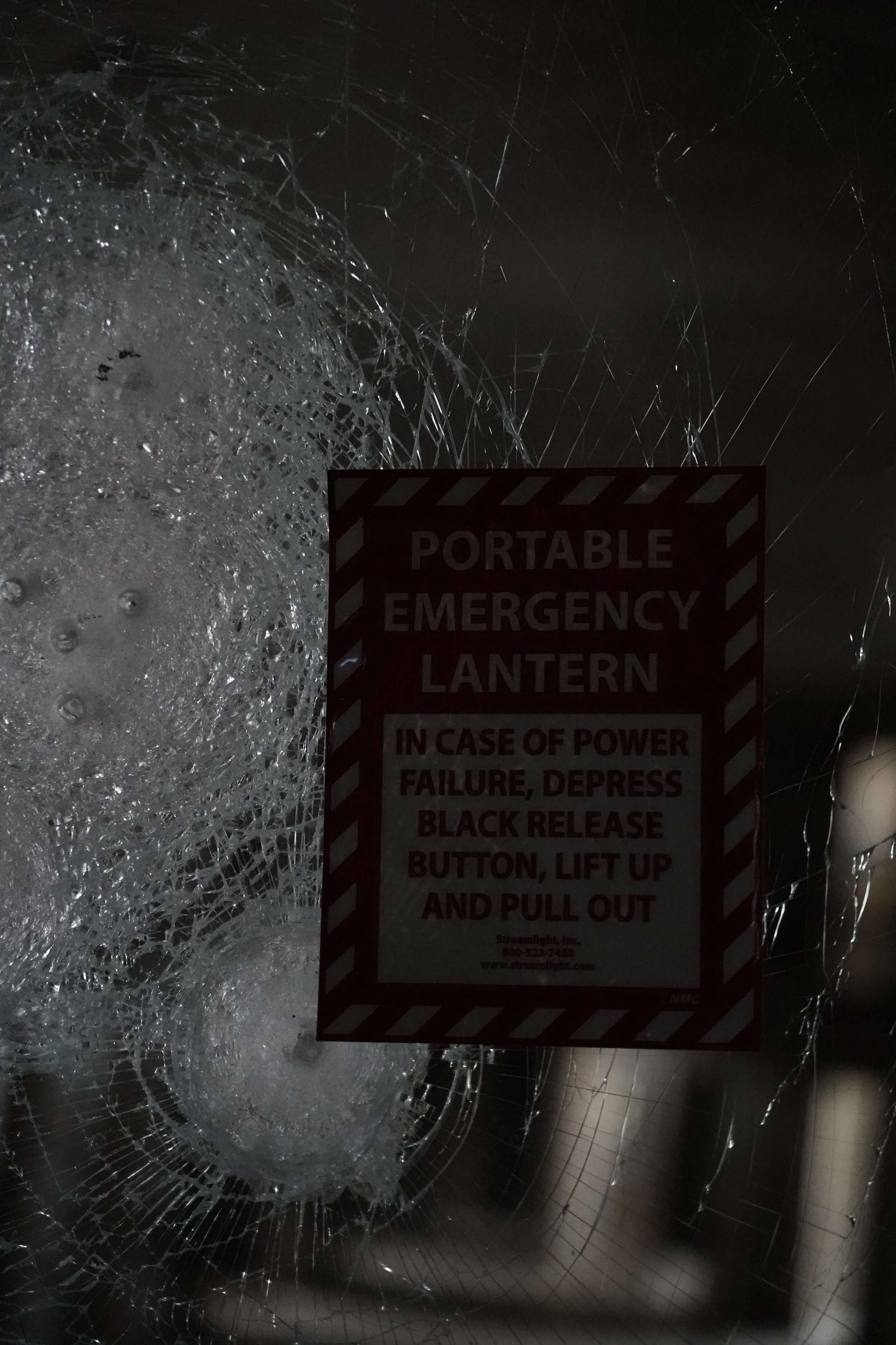 Shattered glass with a safety sign that reads 'Portable Emergency Lantern' in the foreground.