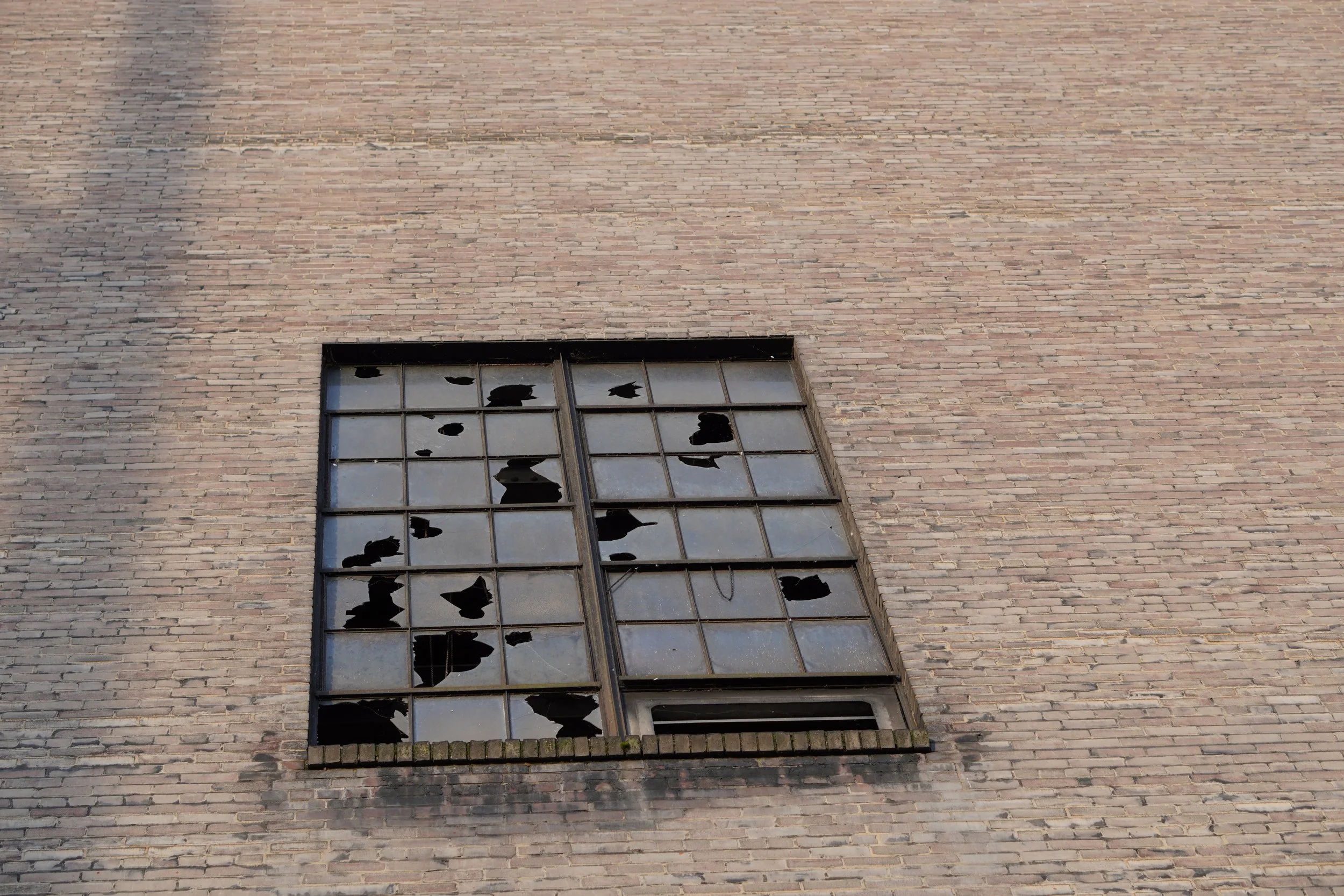 Broken windows with shattered glass in a multi-pane window on a brick building.