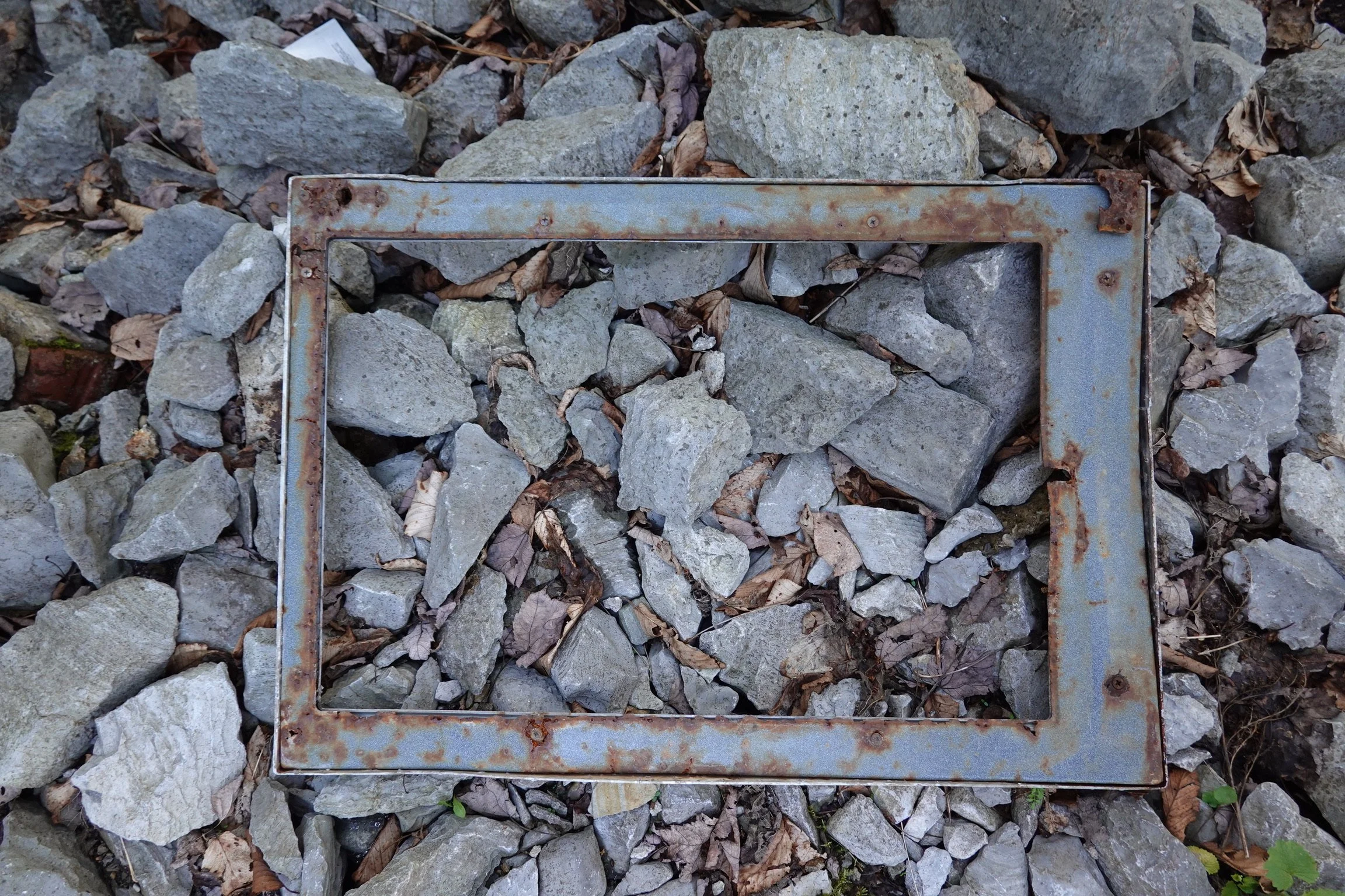 Rusty steel frame lying on a bed of rocks and dry leaves.