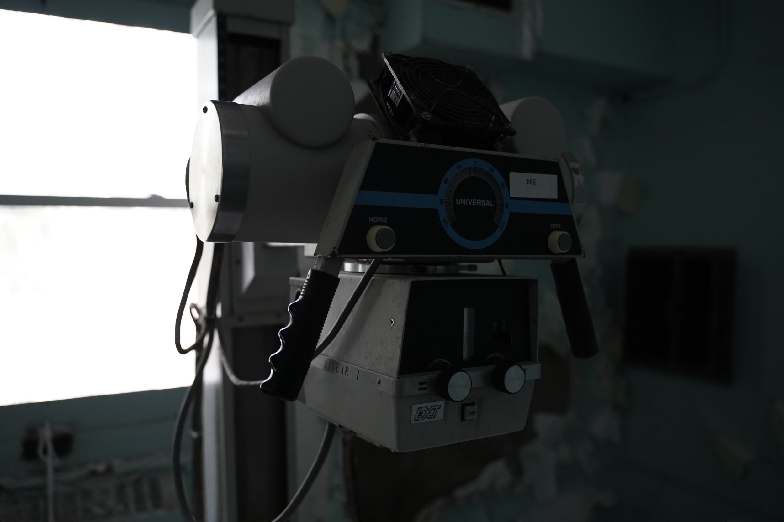 Medical ventilator machine with controls and attached tubing, placed in a dimly lit hospital or medical setting.