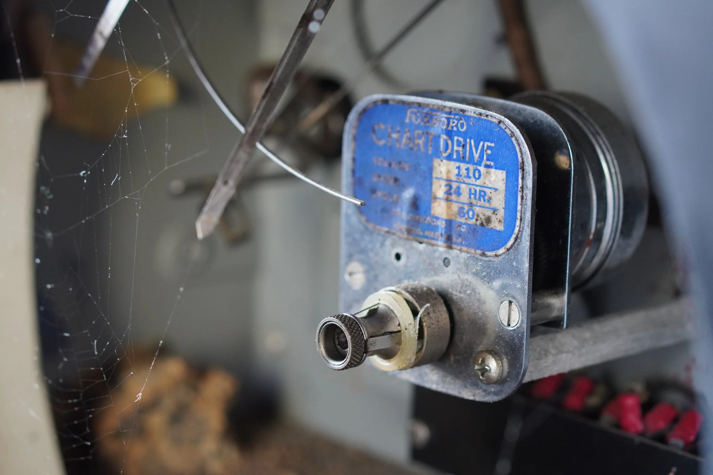 Close-up of a vintage metal project timer labeled 'FazCorpo' with the words 'Chart Drive', speed '110', and '24 HR', in a workshop setting.