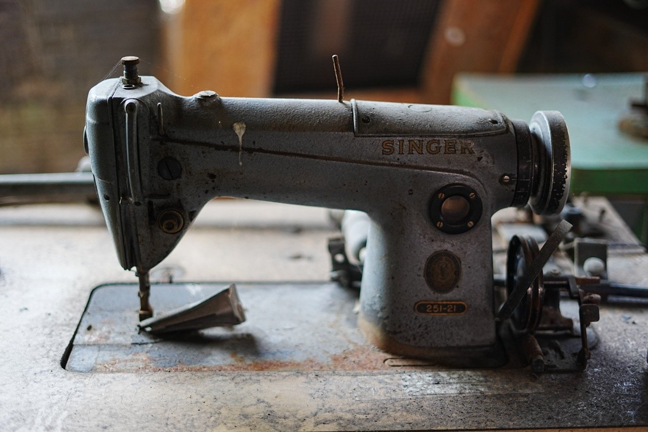 An old, vintage Singer sewing machine with a worn gray finish, placed on a work surface. The machine shows signs of rust and use, with some parts appearing rusted or damaged.