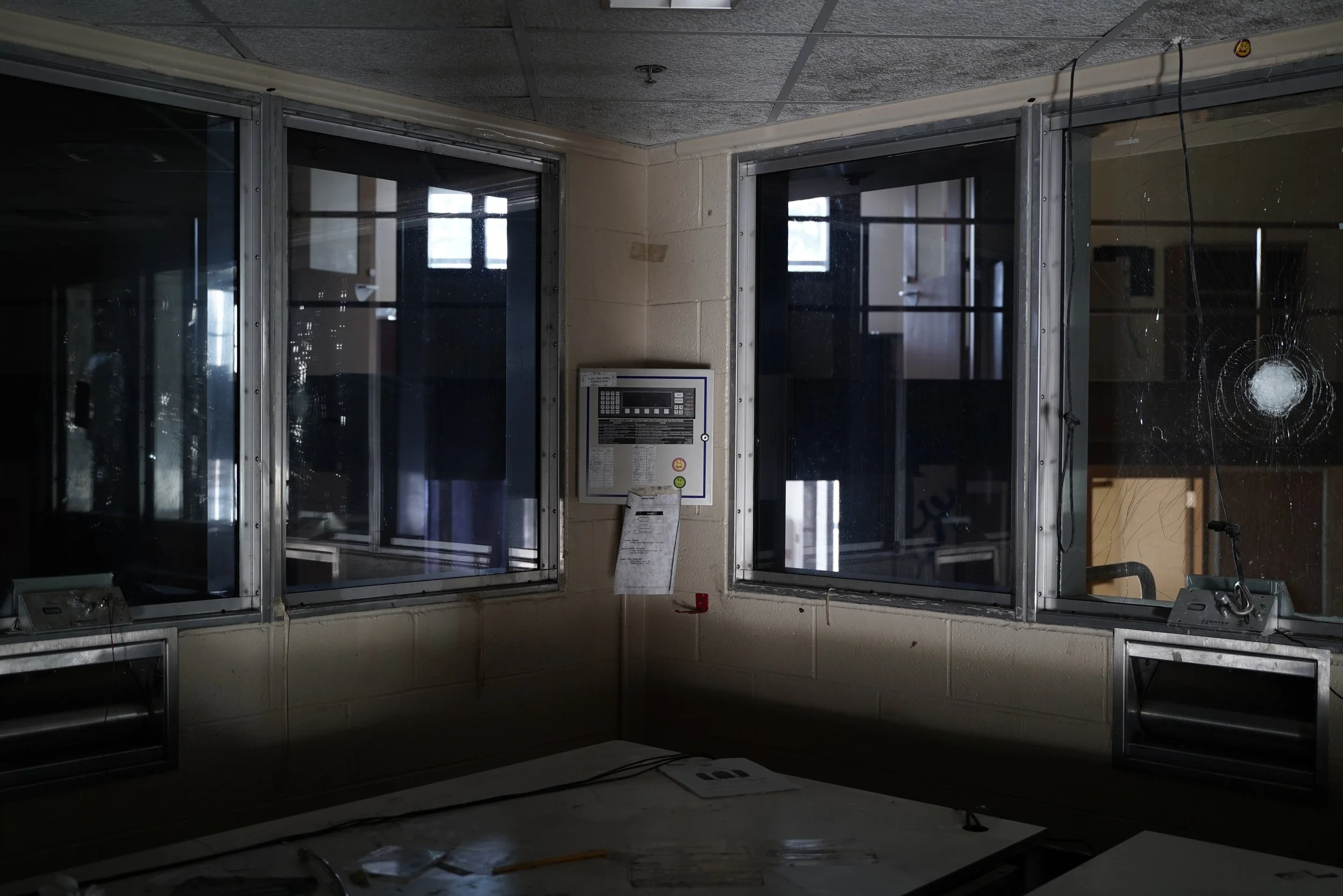 Interior of an abandoned office or security checkpoint with broken glass, spider webs, and disorganized papers.
