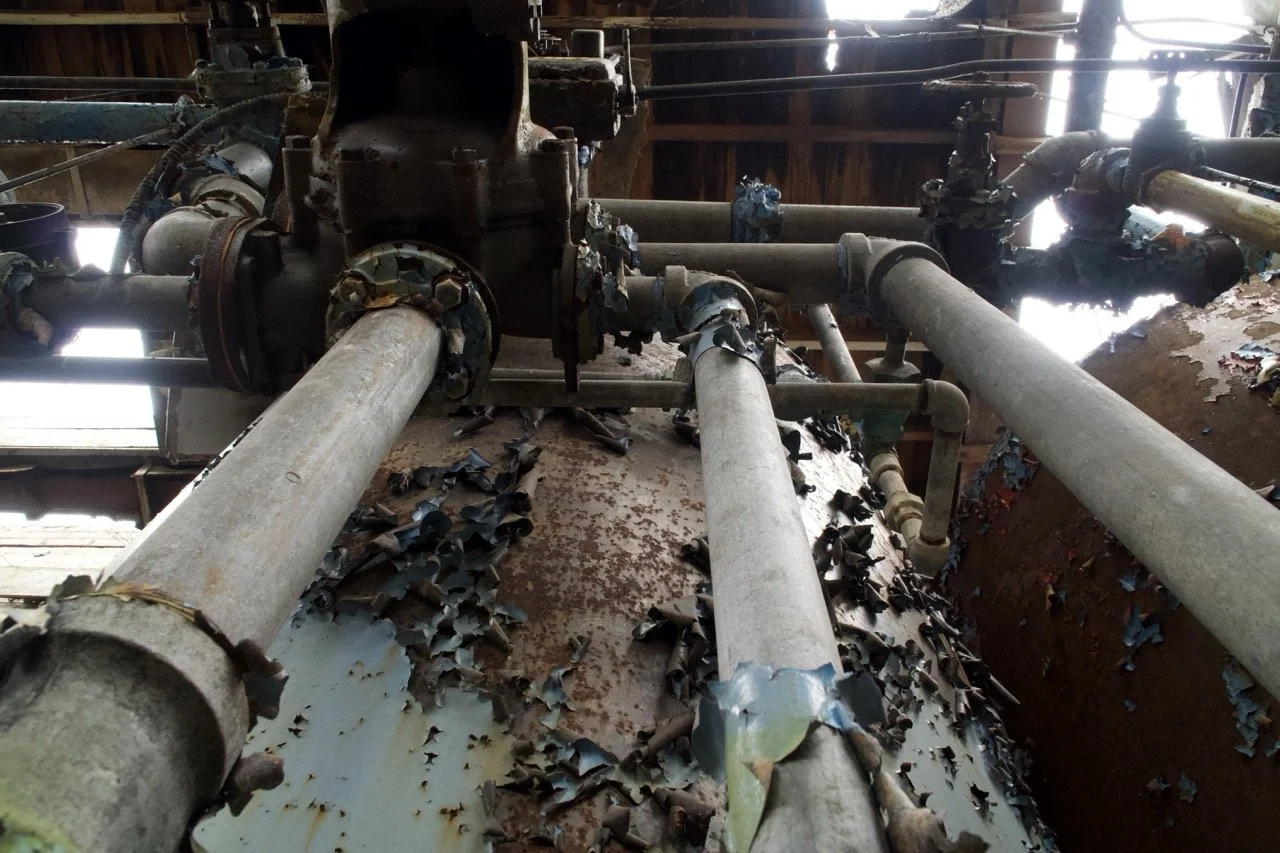 Rusty industrial pipes and machinery with peeling paint and corrosion inside a decayed building