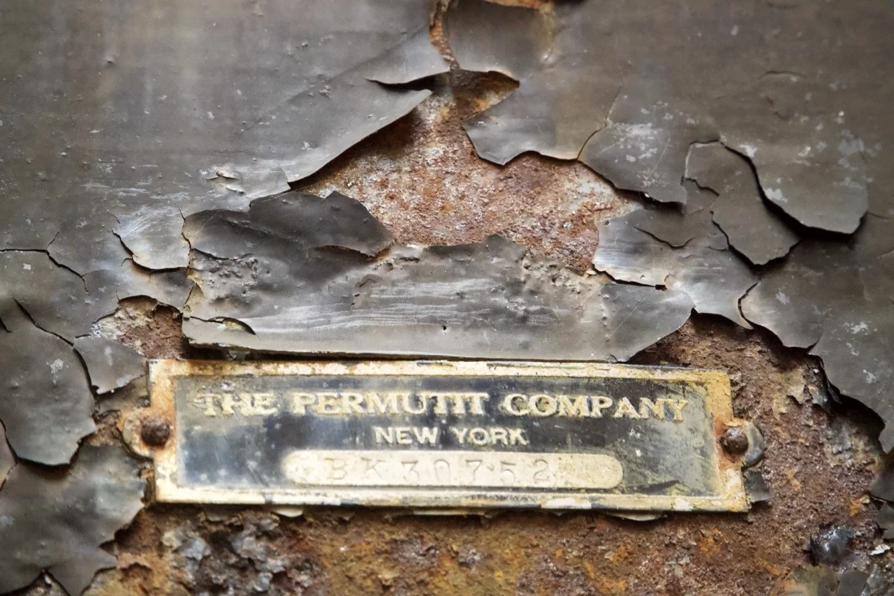 Close-up of a weathered metal surface with peeling paint and a rusted metal plaque that reads "The Permit Company, New York, 38730752."