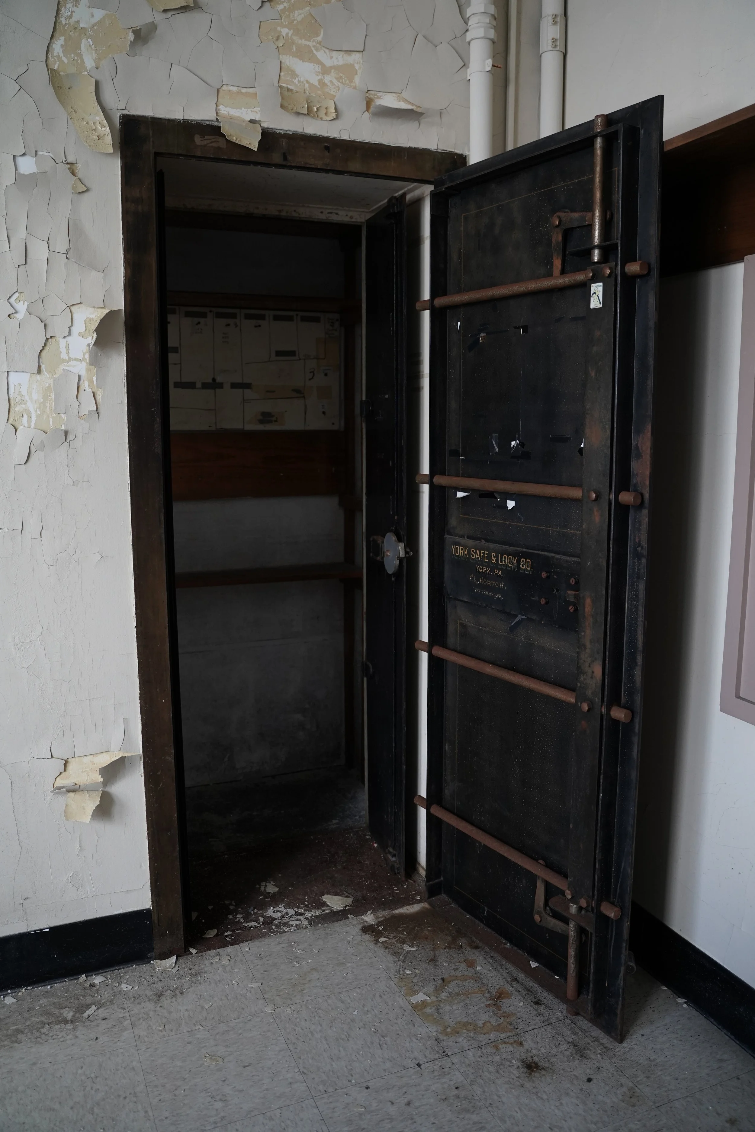 An abandoned, open safe in a room with peeling paint on the walls and debris on the floor.