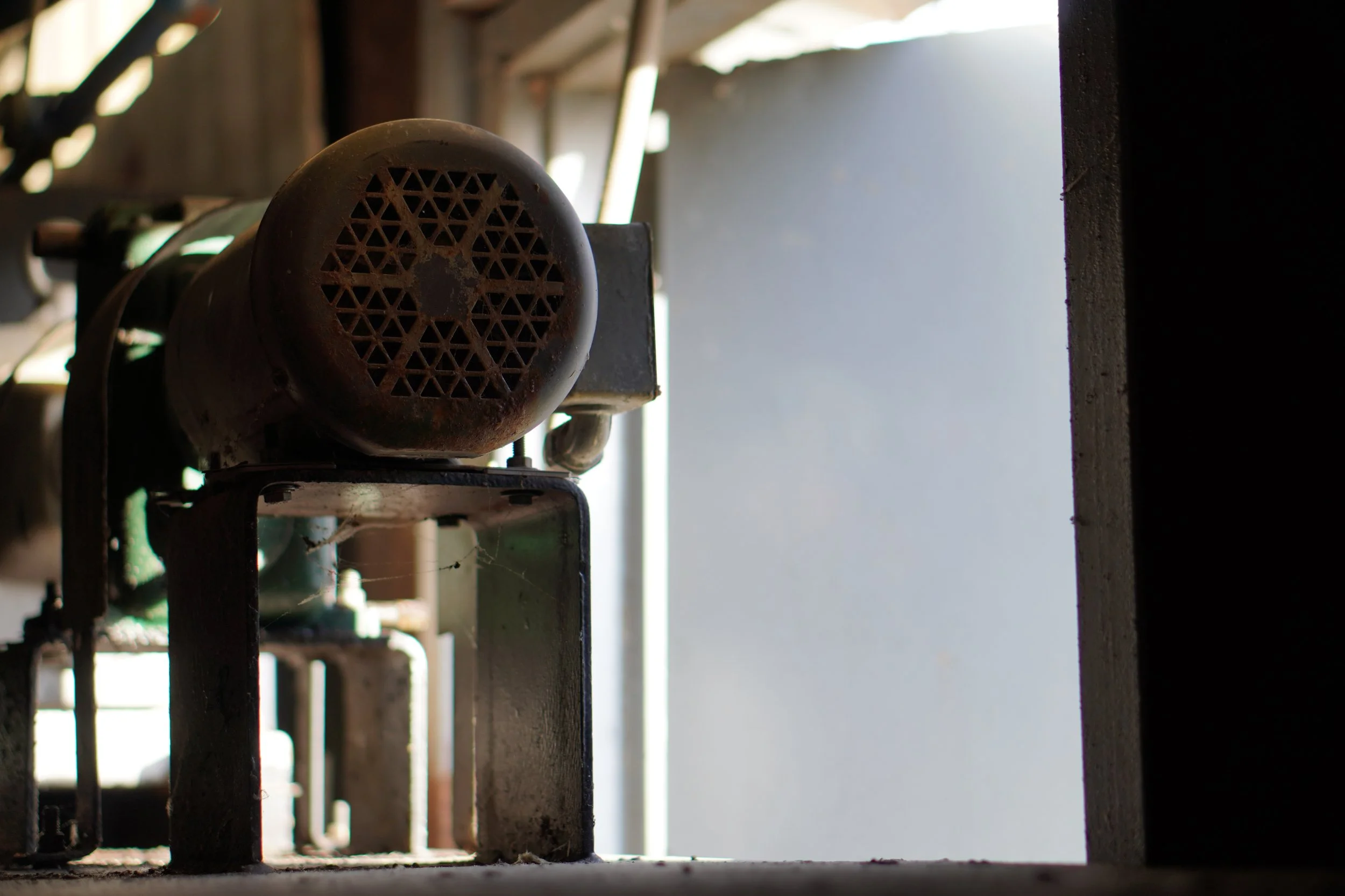 An old rusty metal speaker with a circular grill pattern, mounted on a wall or platform in a rustic setting.