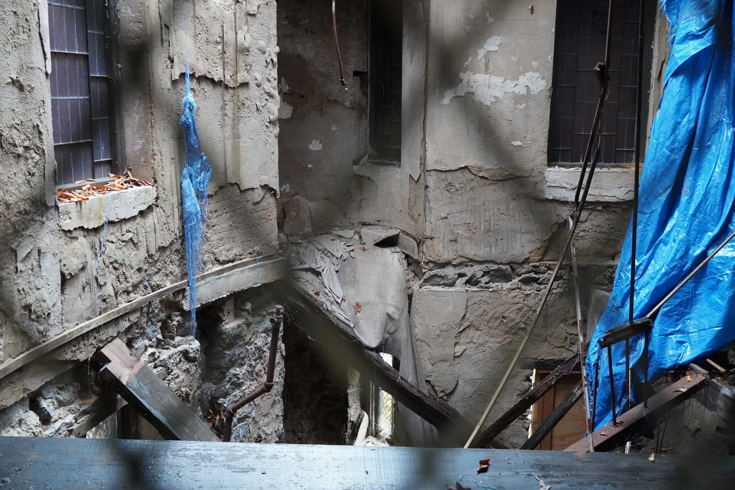 Damage to a building's interior with exposed insulation, bricks, and scattered debris; partially covered with a blue tarp.