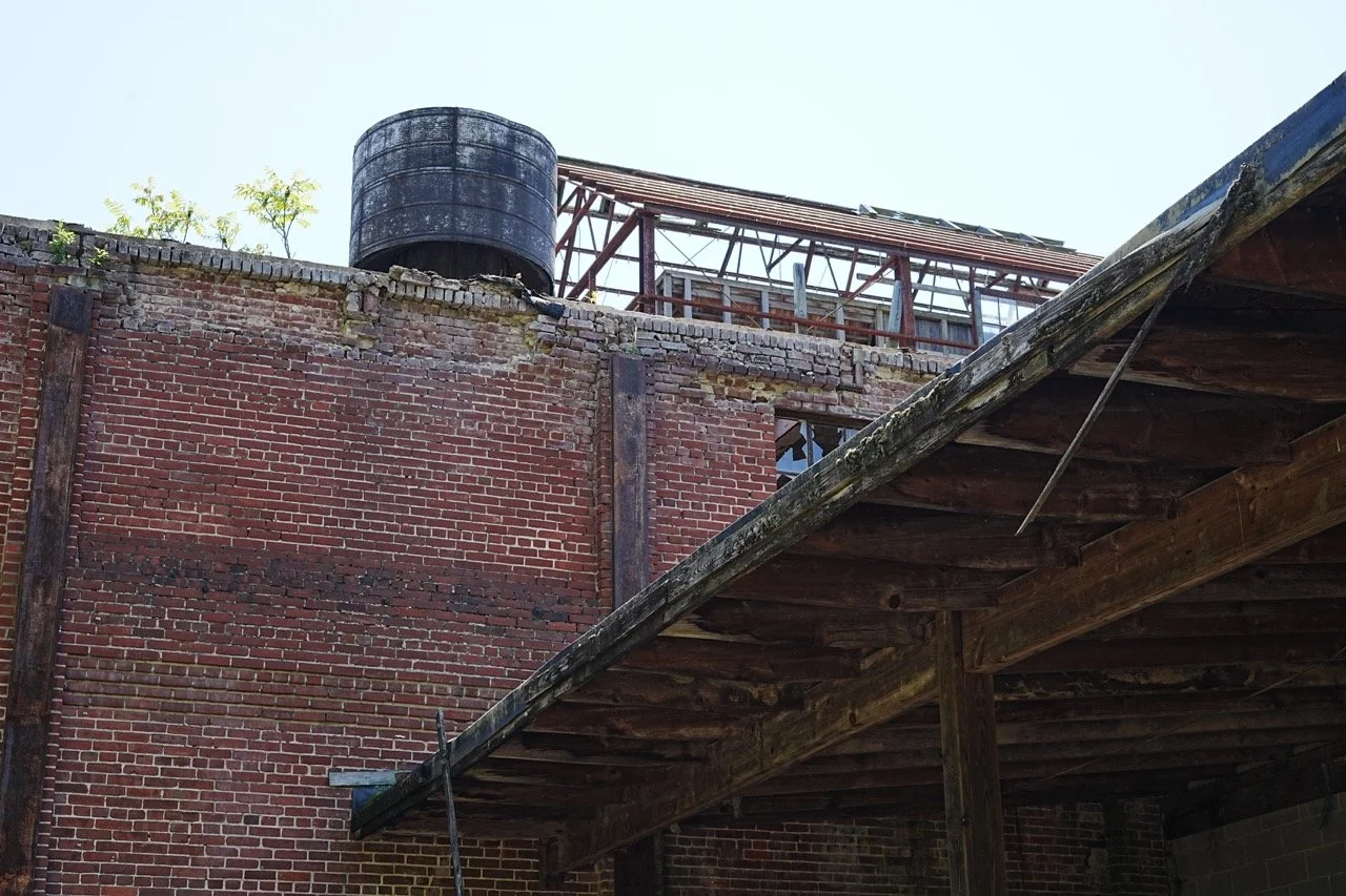 The image shows a brick wall with a water tank and metal structure on top, along with part of a wooden roof extending from the side.