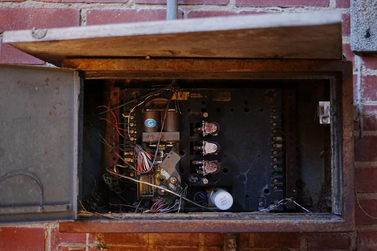 Inside an old, rusted electrical control box mounted on a brick wall, showing wiring and electronic components.