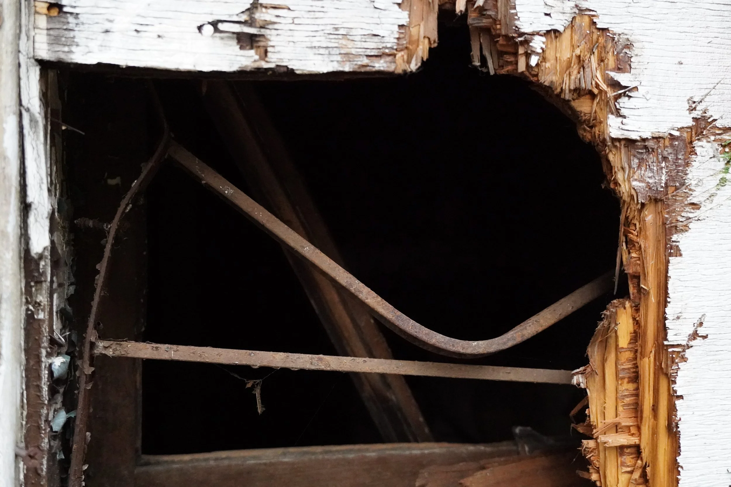 Close-up of a damaged wooden structure with a large hole, revealing rusted metal beams inside.