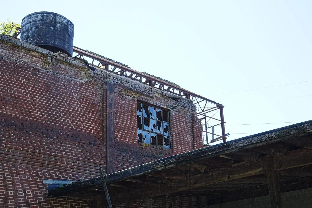 An old red brick building with broken windows and a large black water tank on the roof.