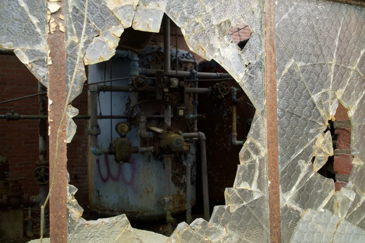 Broken glass window with an industrial boiler or machinery visible through the hole