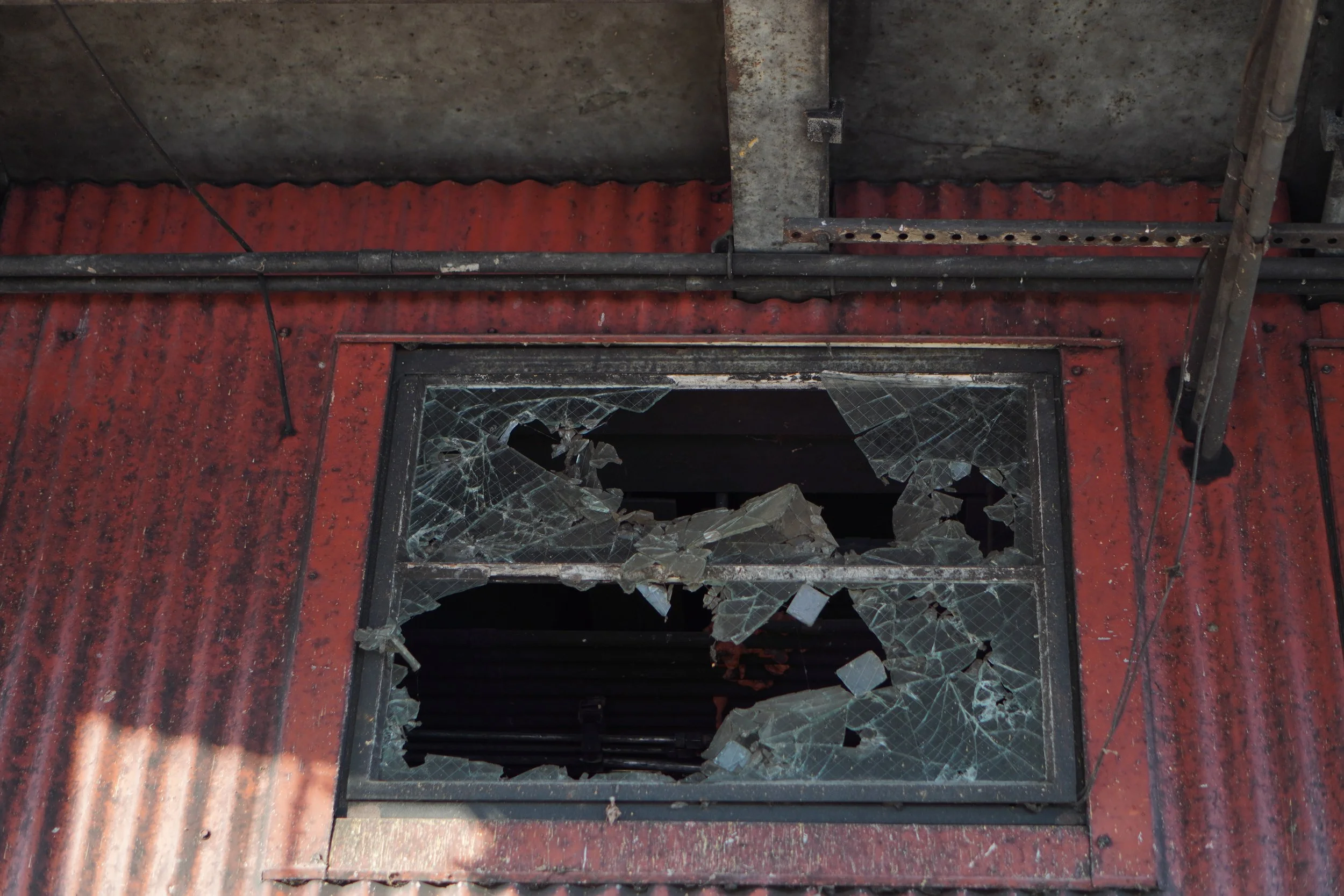 Broken glass window and damaged structure. The window glass is shattered with jagged edges; the surrounding area appears worn and rusty.