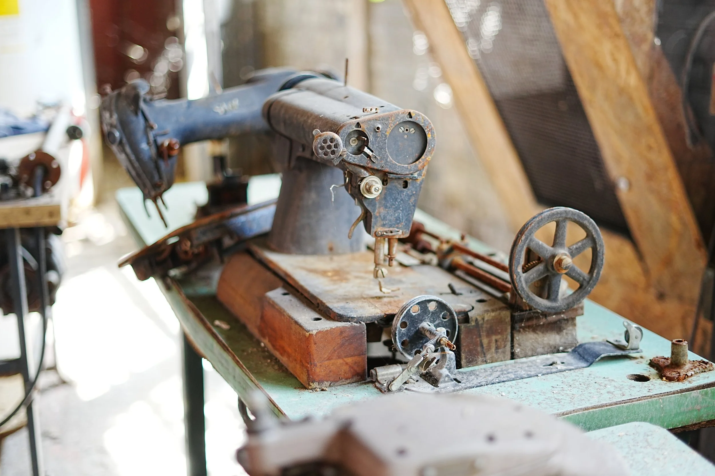 An old, rusty sewing machine on a wooden worktable inside a workshop.