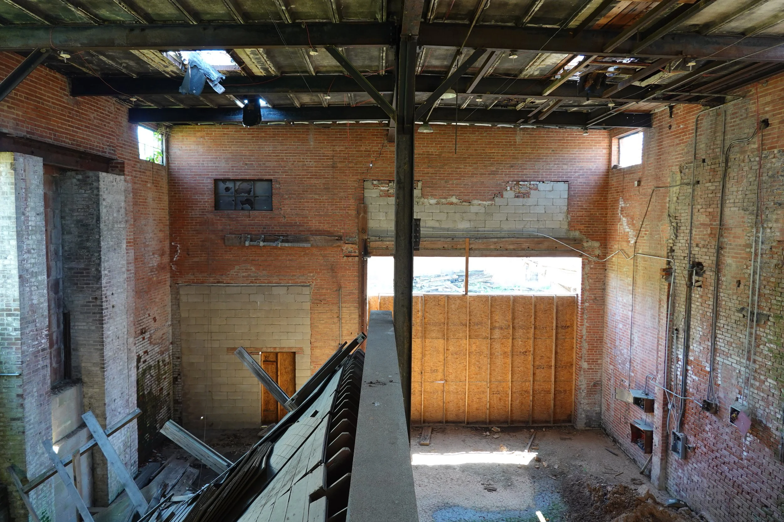 Interior of a building under renovation with exposed brick walls, unfinished ceiling, and construction debris on the floor.