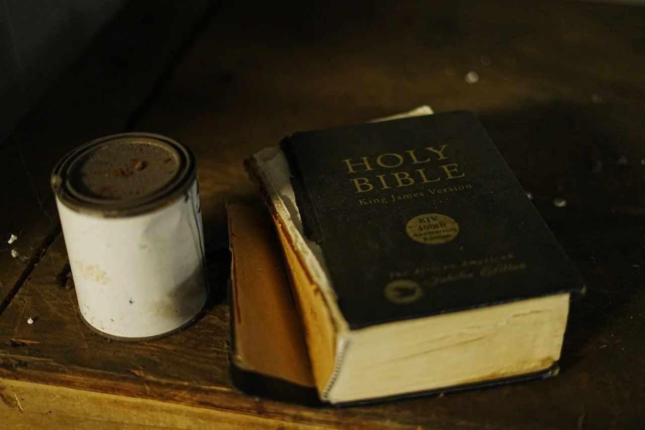 A can of food and a worn Holy Bible with a black cover and gold text on a wooden surface.