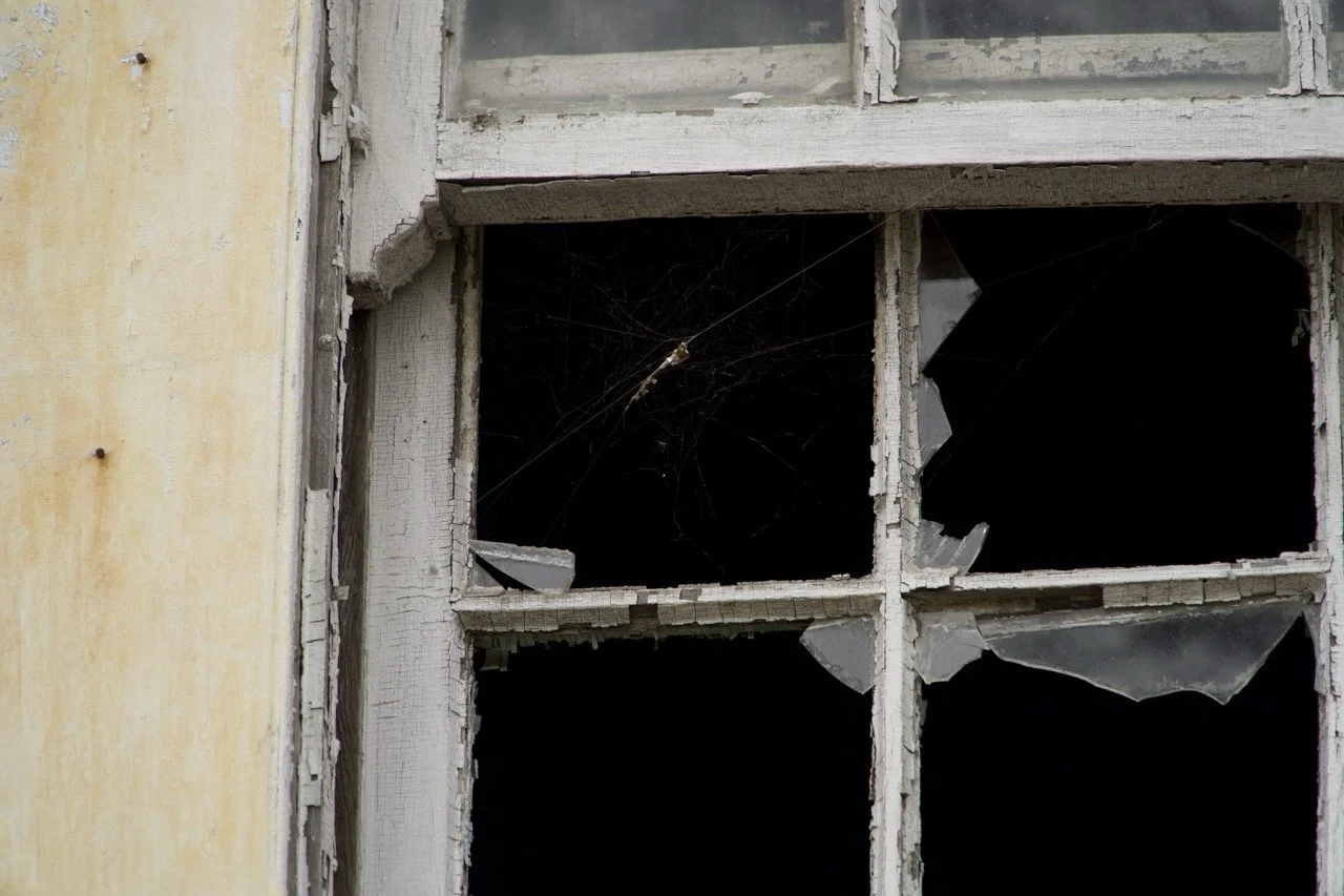 Broken window with shattered glass and spider webs.