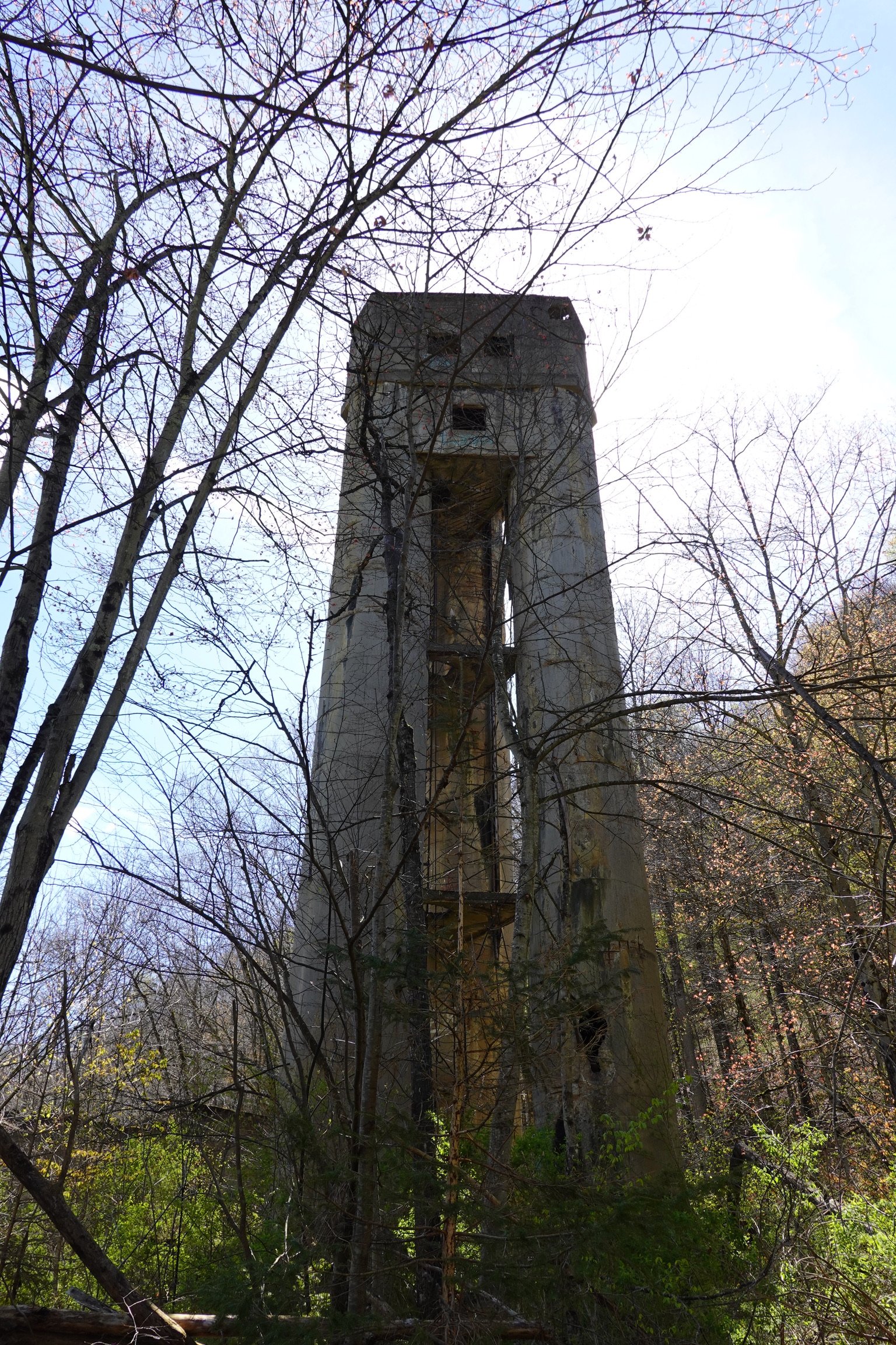 An abandoned concrete tower with broken windows, surrounded by leafless trees in a forest.